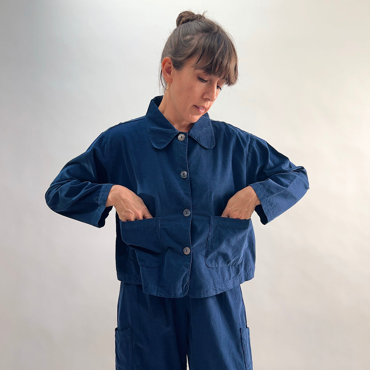 Model with hands in patch pockets of the Bryn Walker Corduroy Audrey Jacket in Nova, front view showing rounded collar, shell buttons, and navy pinwheel corduroy texture

