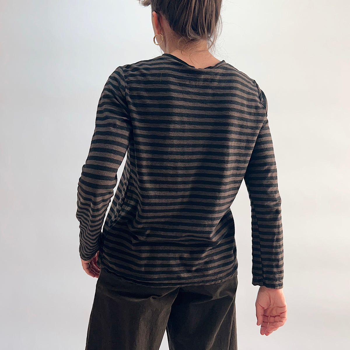 Back view of the Cut Loose Striped Long Sleeve Easy Tee in Chocolate, showing the relaxed easy fit, long sleeves, and slightly curved hem in a lightweight chocolate and black horizontal stripe cotton-linen blend, paired with dark wide-leg crop trousers
