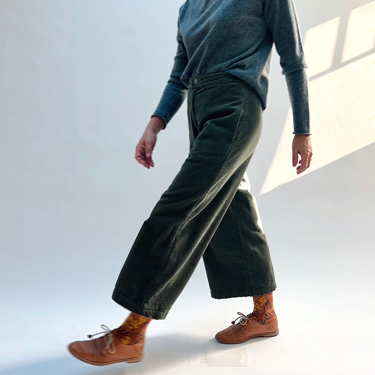 Side view of a model walking in the Lux Corduroy Crop Wide Leg Pant in Kelp, showing the wide legs in motion.
