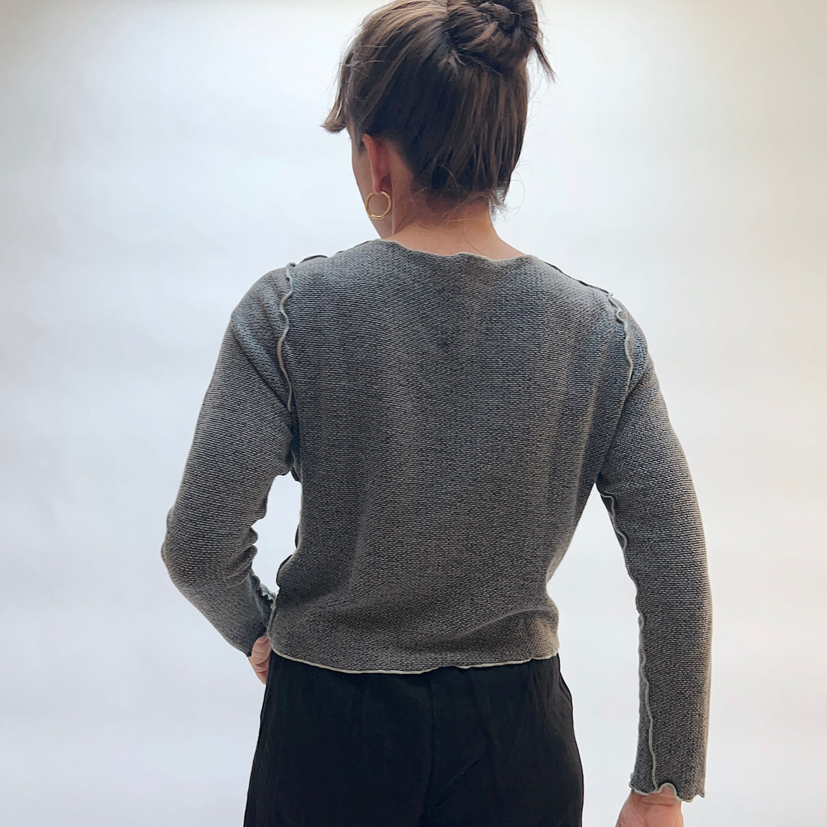 Model wearing the Marled Knit Cropped Cardigan in Squirrel, back view, showing cropped silhouette and scalloped hem and cuffs in heathered gray marled knit
