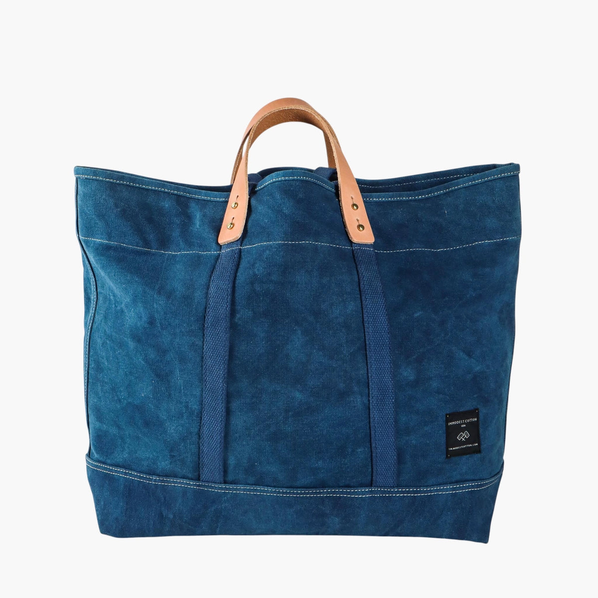 Immodest Cotton Large East West Tote in Indigo with short natural leather handles and contrast stitching.
