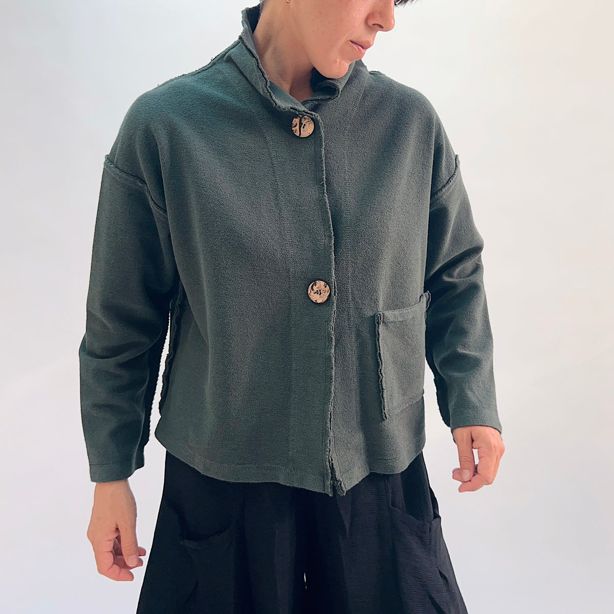 Eleven Stitch Funnel Jacket in Konbu, front view showing the two large wooden buttons, high funnel collar with raw-edge trim, and large hip patch pocket in forest green cotton terry
