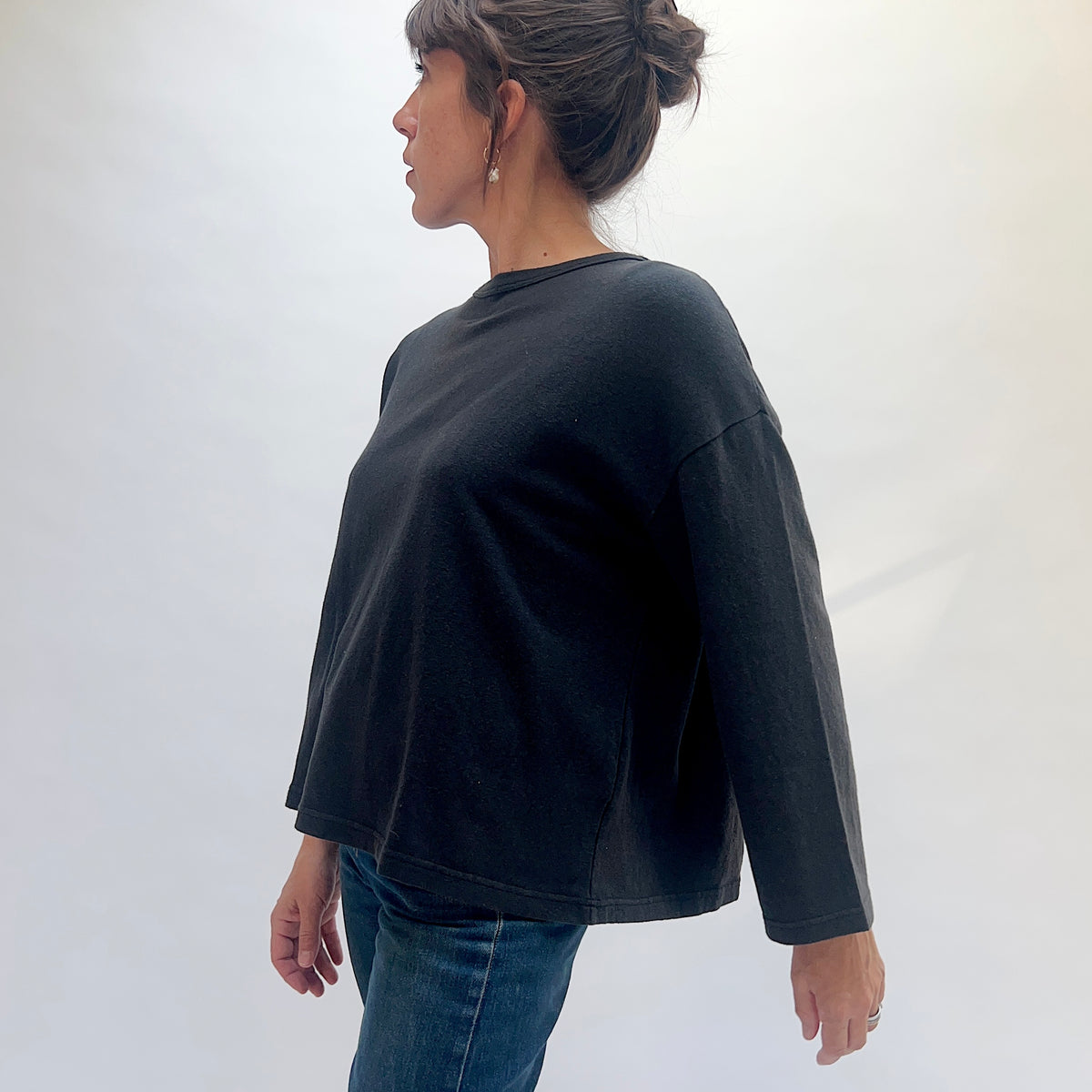 Angled view of a model wearing the black cotton knit pullover, showing the dropped shoulder, sleeve, and side seam.
