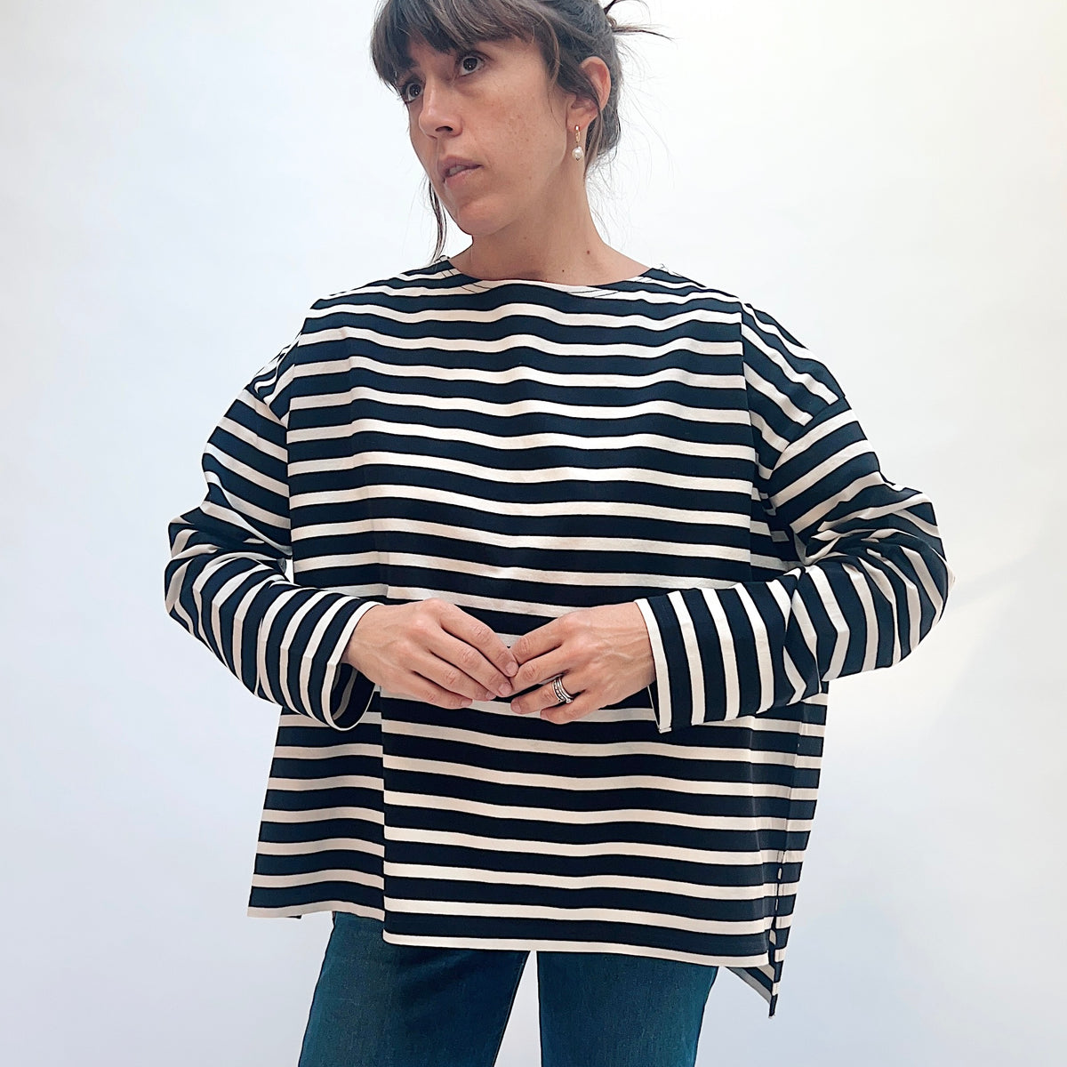 Model wearing the black and natural striped knit pullover with hands together, showing the horizontal stripes across the front.
