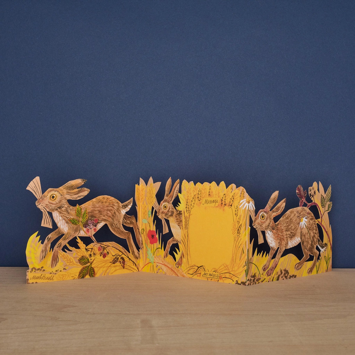 Hares Collage concertina card open to reveal blank message panel, with illustrated hares and meadow botanicals on either side, signed by Mark Hearld and Art Angels