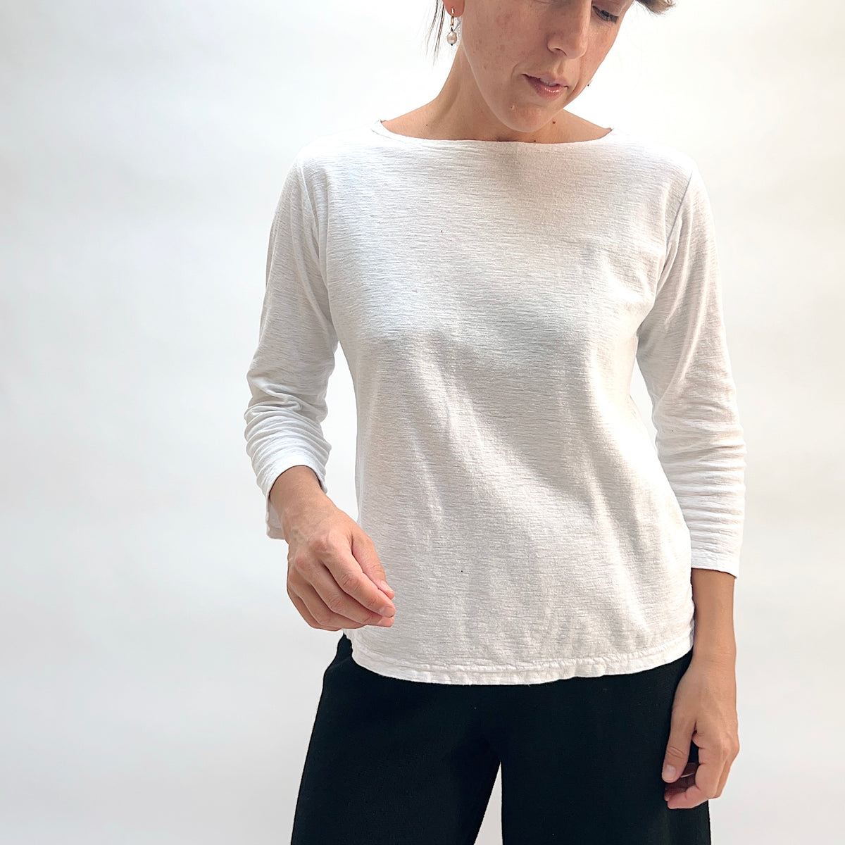 Model wearing the Cut Loose 3/4 Sleeve Boatneck Top in White, full-length front view looking down, showing relaxed straight hem and wide boatneck neckline of white cotton-linen top with 3/4 sleeves, styled with black pants
