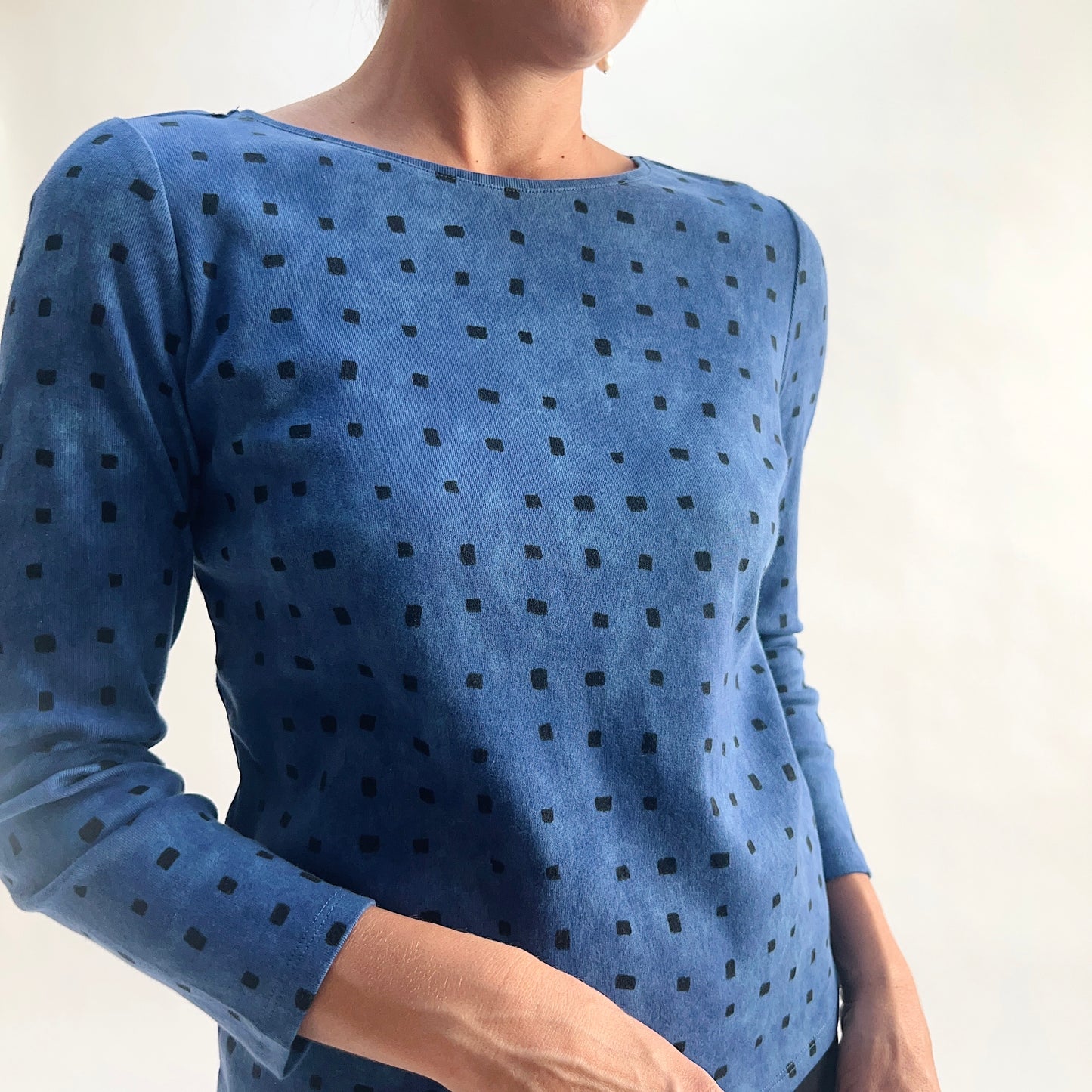 Close front view of model wearing a medium indigo long-sleeve cozy rib tee with all-over tonal dark navy square print, showing the scoop neckline, rib knit texture, and square print detail against a white background.

