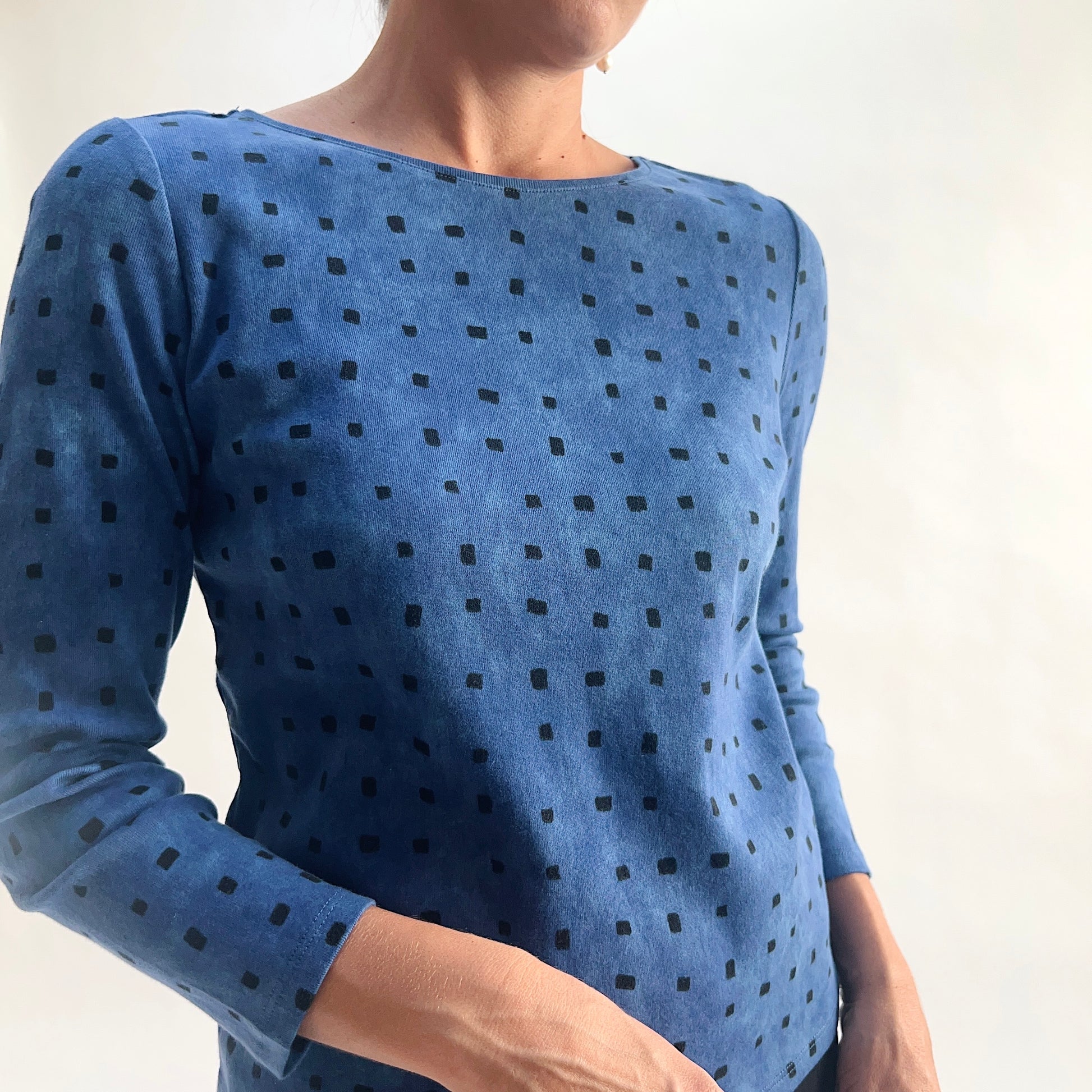 Close front view of model wearing a medium indigo long-sleeve cozy rib tee with all-over tonal dark navy square print, showing the scoop neckline, rib knit texture, and square print detail against a white background.
