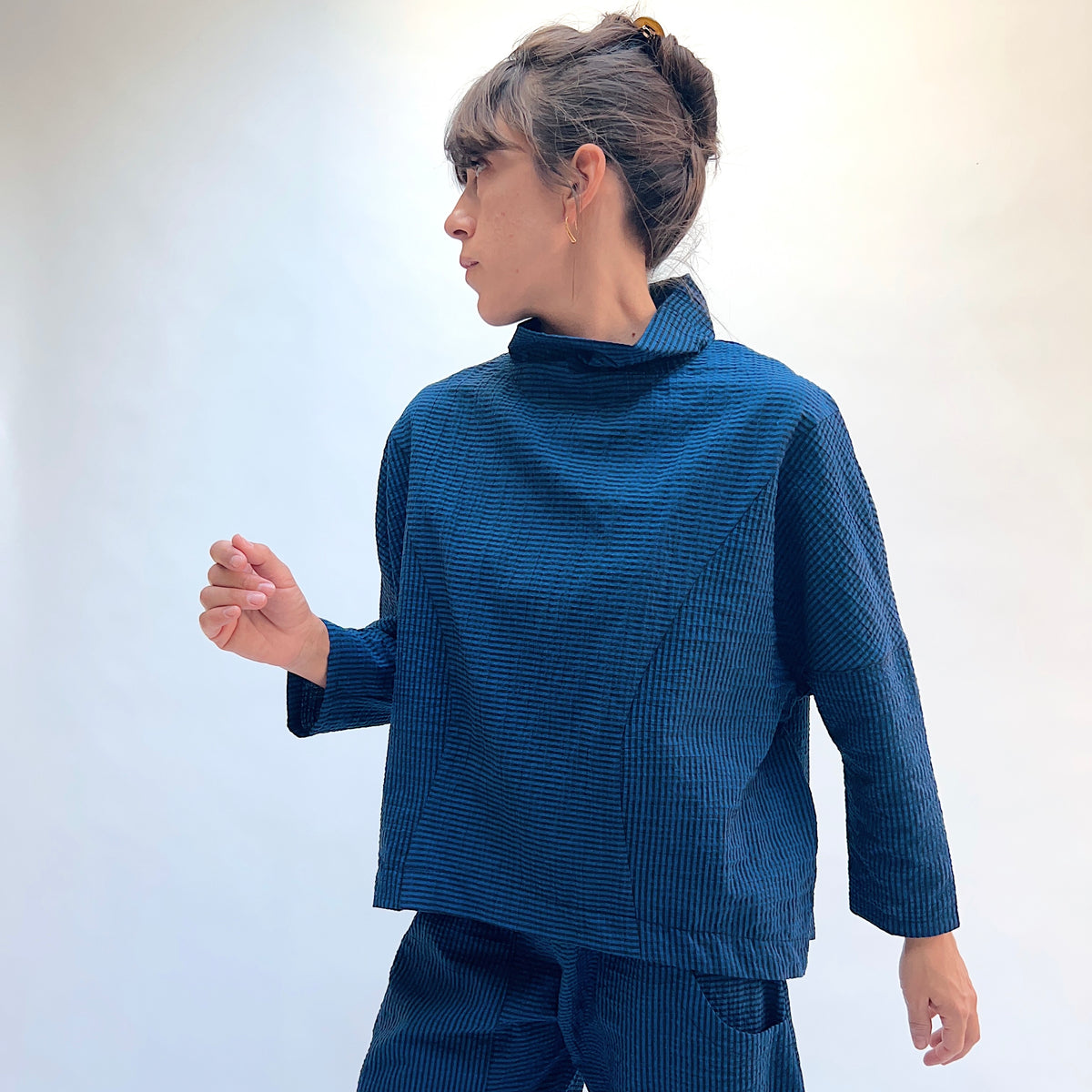 Niche Sofi Top in Blue Seersucker Stripe, side view showing the relaxed boxy silhouette and high funnel neck in teal and black seersucker stripe
