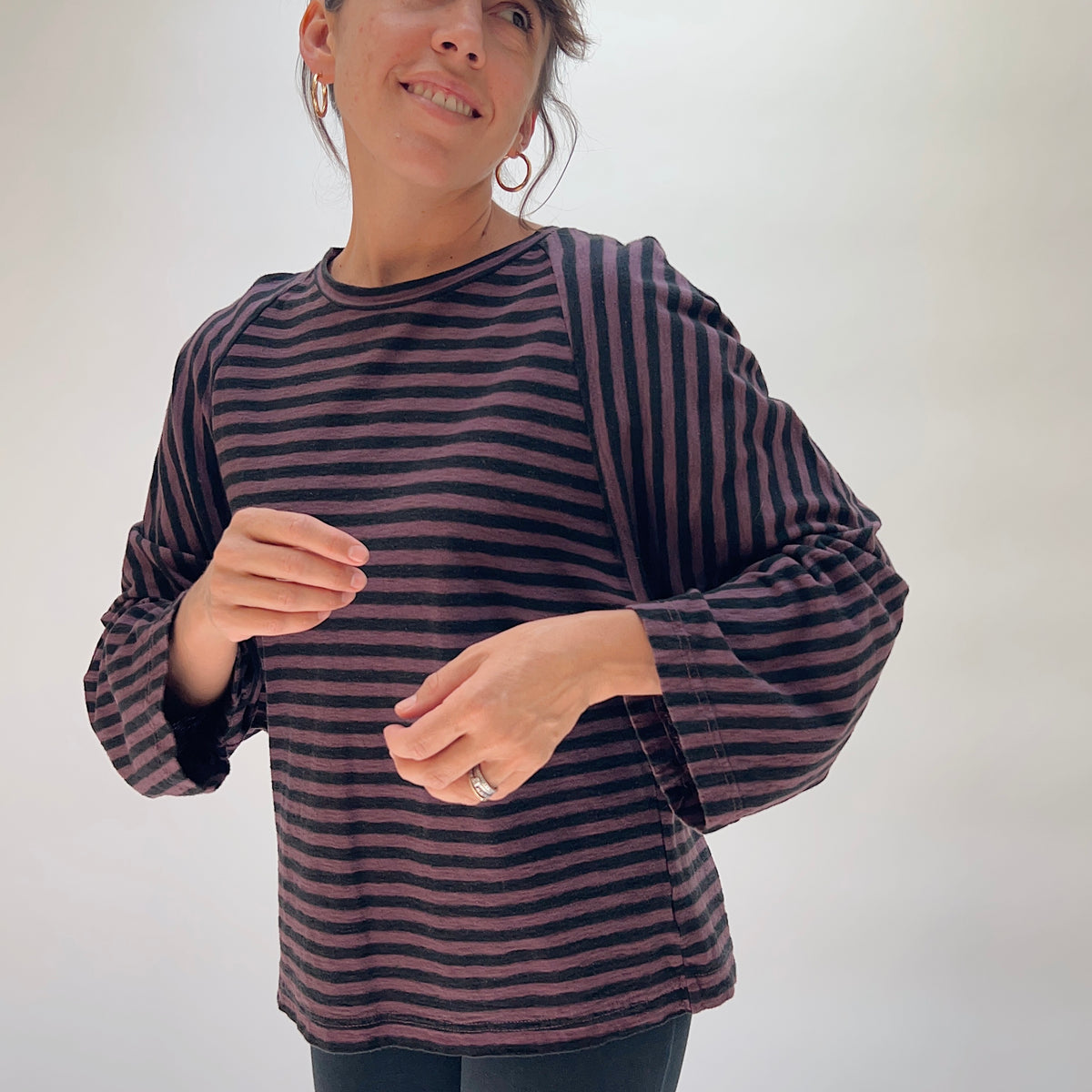 Model wearing the Cut Loose Slouchy Raglan Tee in Cinnabark Stripes, shown from a slight front angle — an oversized drop-shoulder raglan tee in horizontal cinnabark and black stripes with wide long sleeves and a crew neckline, in a warm cotton-linen blend
