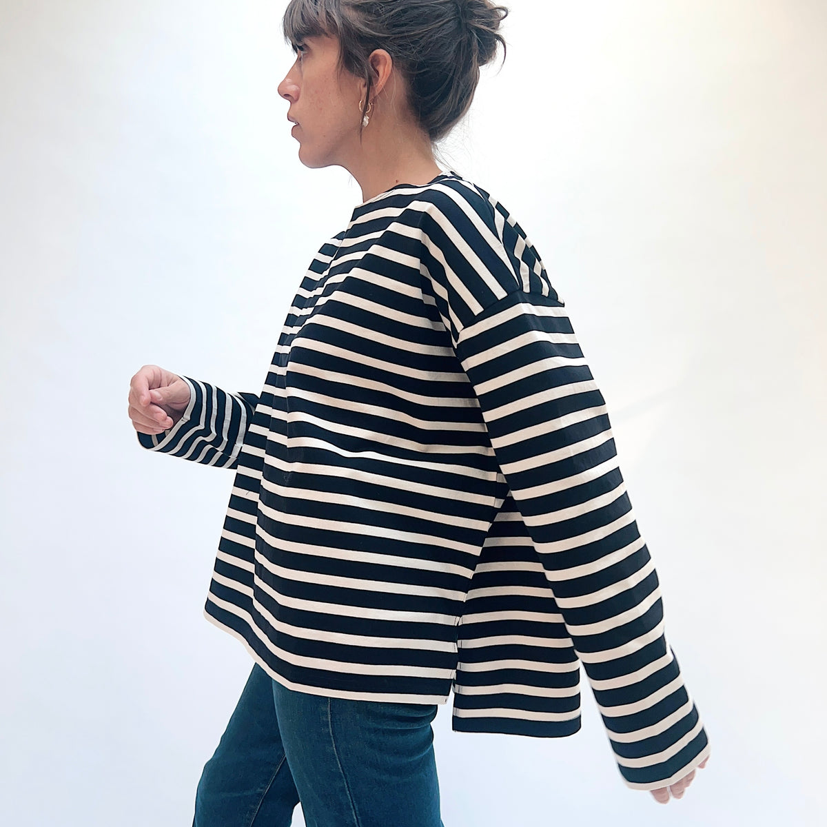 Side view of the black and natural striped knit pullover, showing the dropped shoulder and split hem with a longer back.
