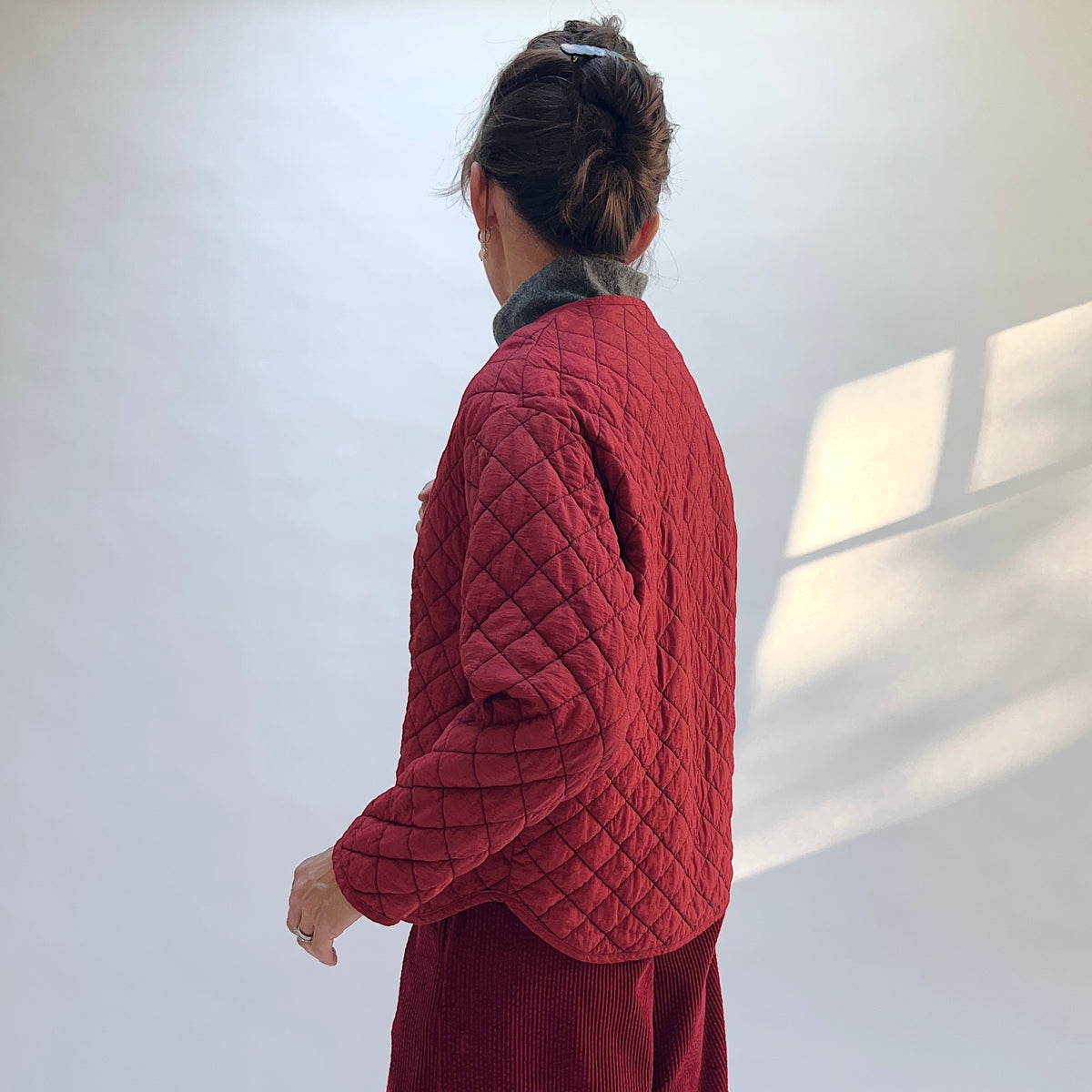 Side and back view of the Quilted Bomber Jacket in Maraschino on a model, showing diamond quilting across the back and sleeves.
