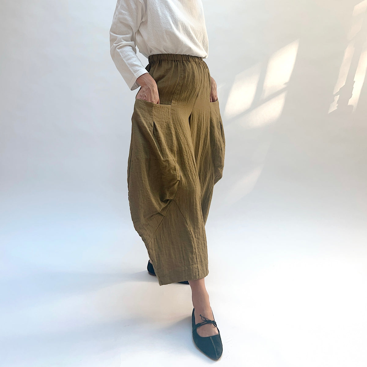 Eleven Stitch Double Pocket Crinkle Travel Pant in Olive, angled view with model's hands in the side pockets.
