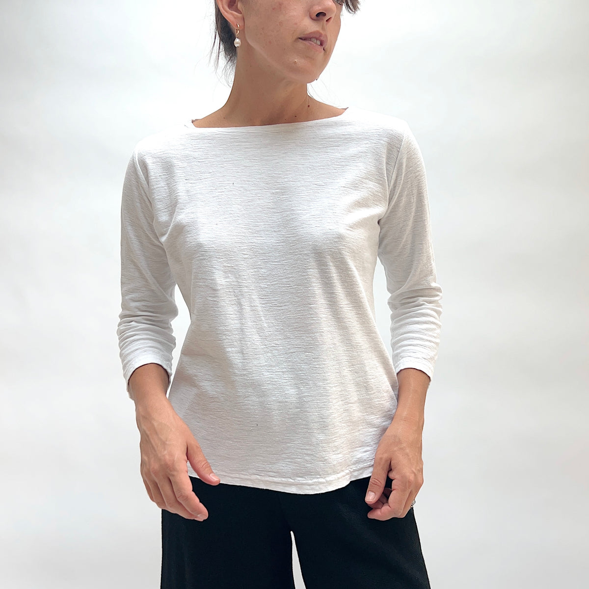 Model wearing the Cut Loose 3/4 Sleeve Boatneck Top in Etan, close-up three-quarter view looking down, deep teal cotton-linen boatneck top with 3/4 sleeves and subtle slub texture, styled with black textured pants
