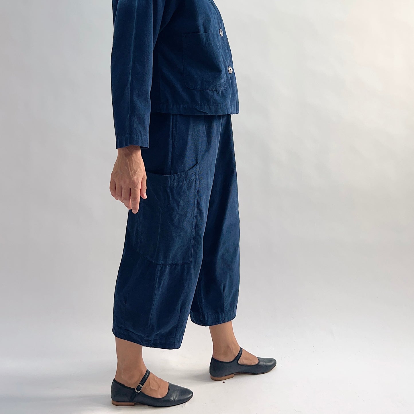 Side view of the Bryn Walker Corduroy Pasha Pants in Nova, showing relaxed wide-leg silhouette, side leg pocket, elastic waistband, and cropped hem in navy pinwheel corduroy, with black Mary Jane flats
