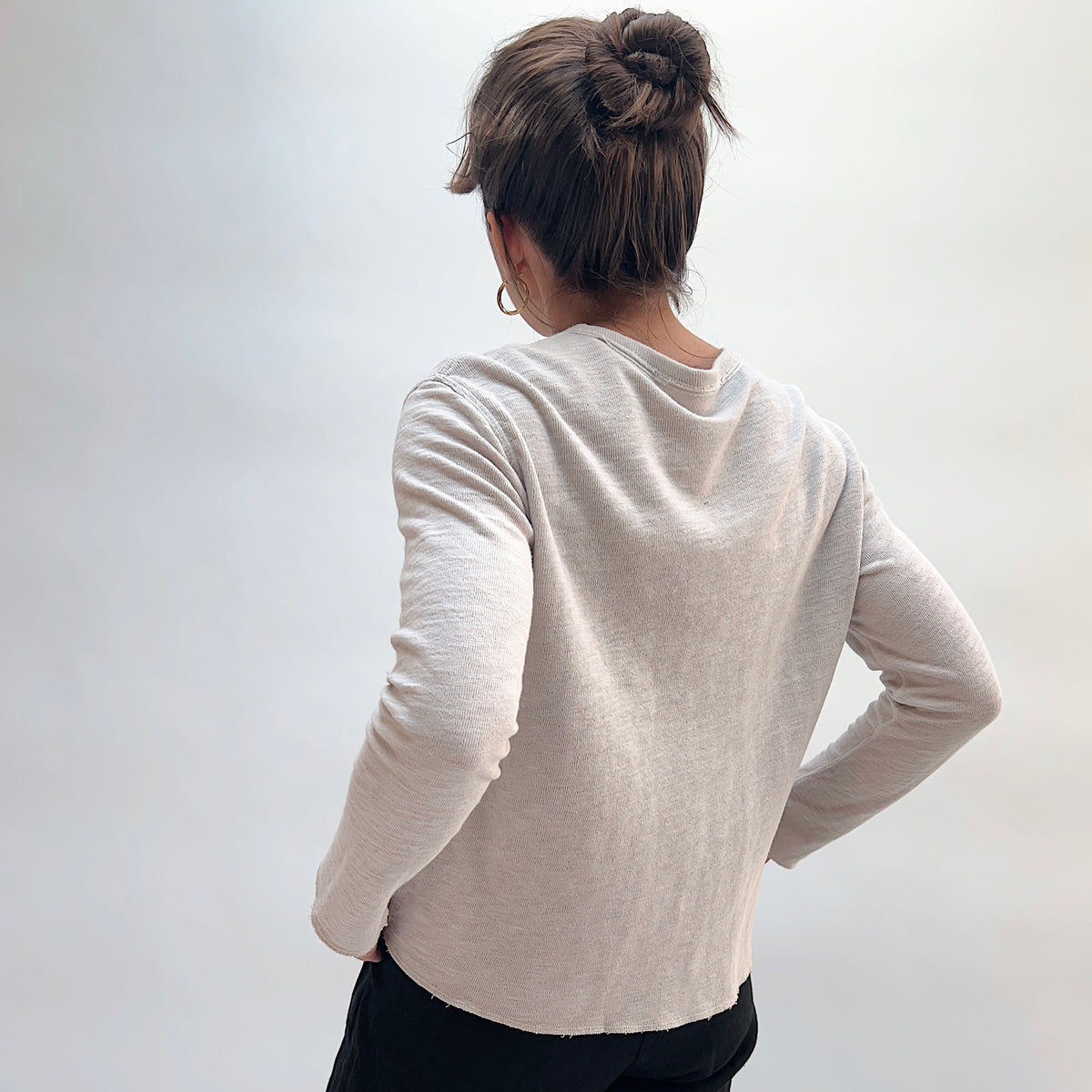 Model wearing the Cut Loose Snap Front Cardigan in Nimbus, back view, showing relaxed silhouette and raw curved hem in light heathered gray cotton
