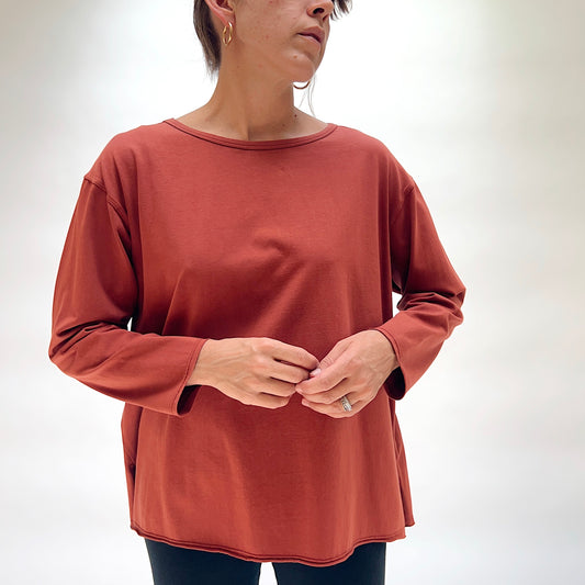 North Star Base Cotton Jersey Beach Tee in Ginger Spice, close front view on model, ginger spice red-brown cotton jersey with boat neckline with lettuce edge, dropped shoulders, and long sleeves with lettuce-edge cuffs, paired with dark jeans
