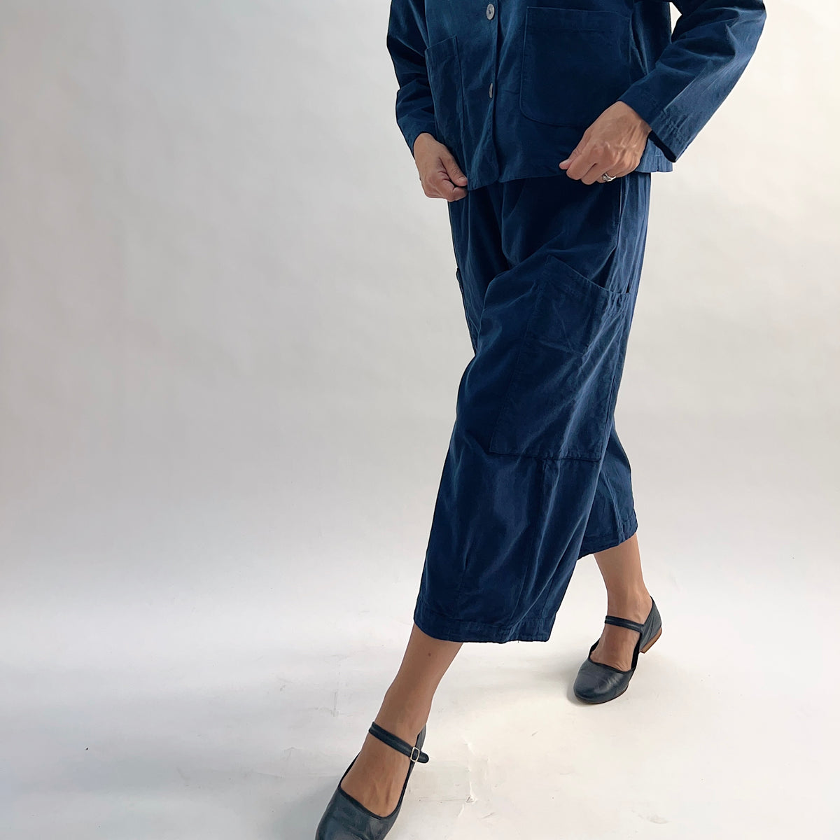 Model in motion wearing the Bryn Walker Corduroy Pasha Pants in Nova, angled front view highlighting side leg pocket detail and navy pinwheel corduroy texture, paired with matching jacket and black flats

