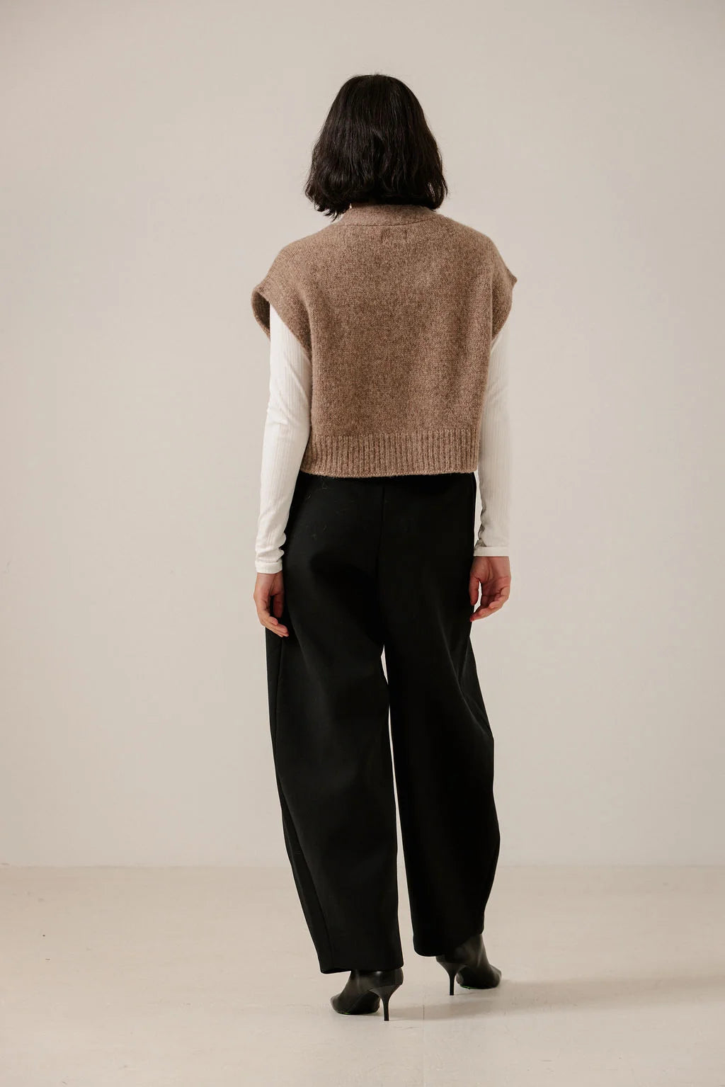 Back view of the Dark Fawn vest on a model, showing its boxy shape, knit texture and ribbed hem.
