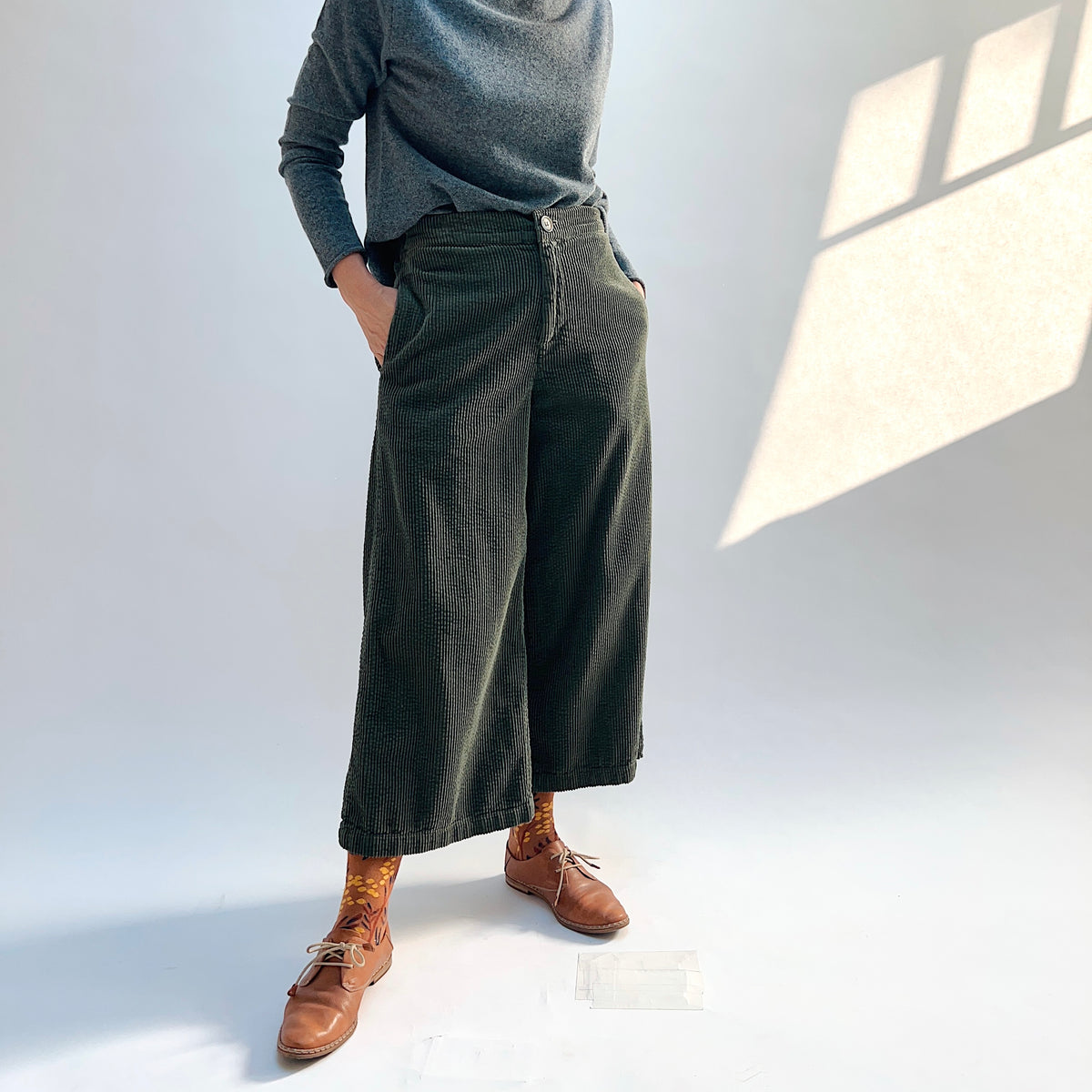 Angled front view of the Lux Corduroy Crop Wide Leg Pant in Kelp, with the model’s hands in the side pockets.
