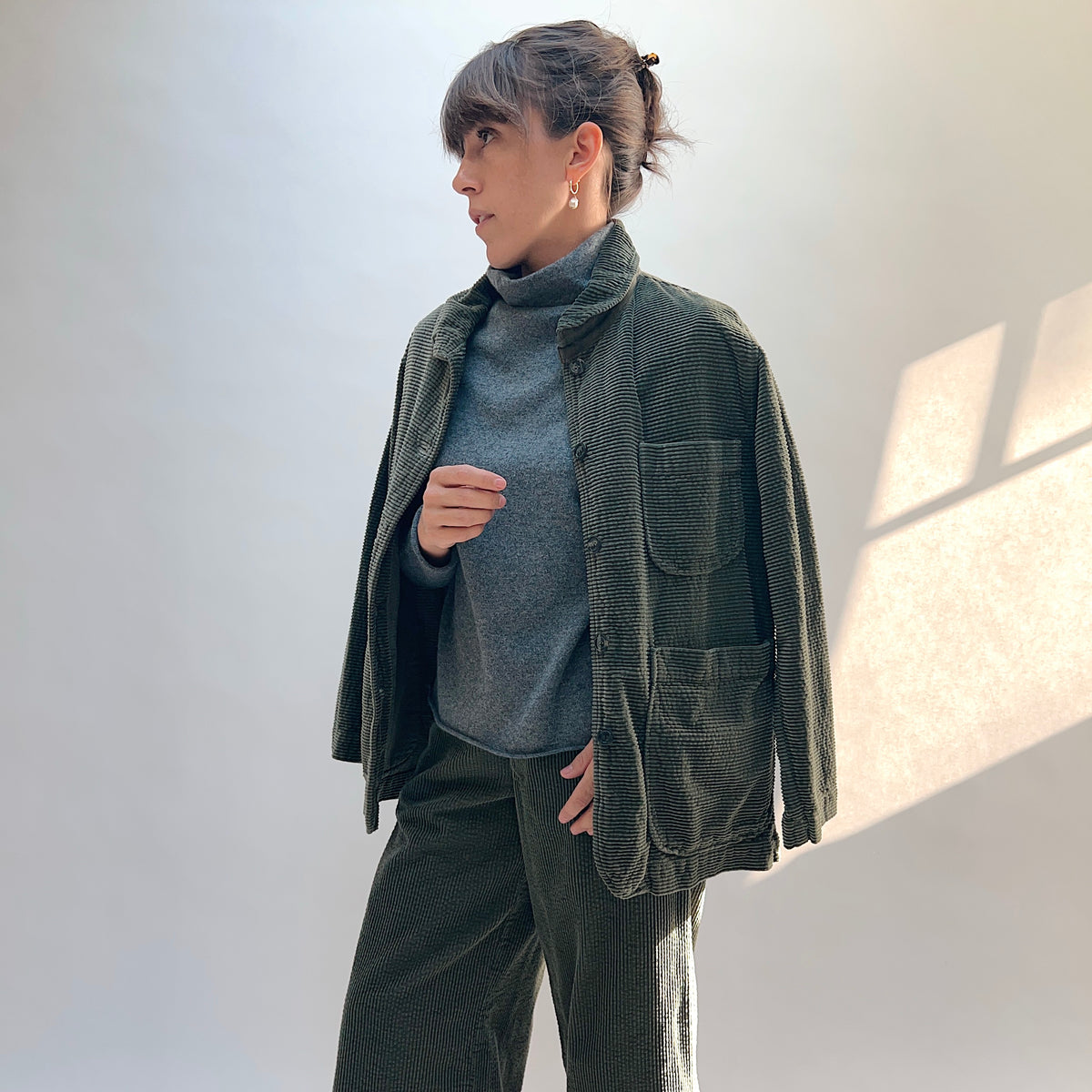 Model wearing the Lux Corduroy Long Blazer in Kelp draped over the shoulders and open over a gray top.
