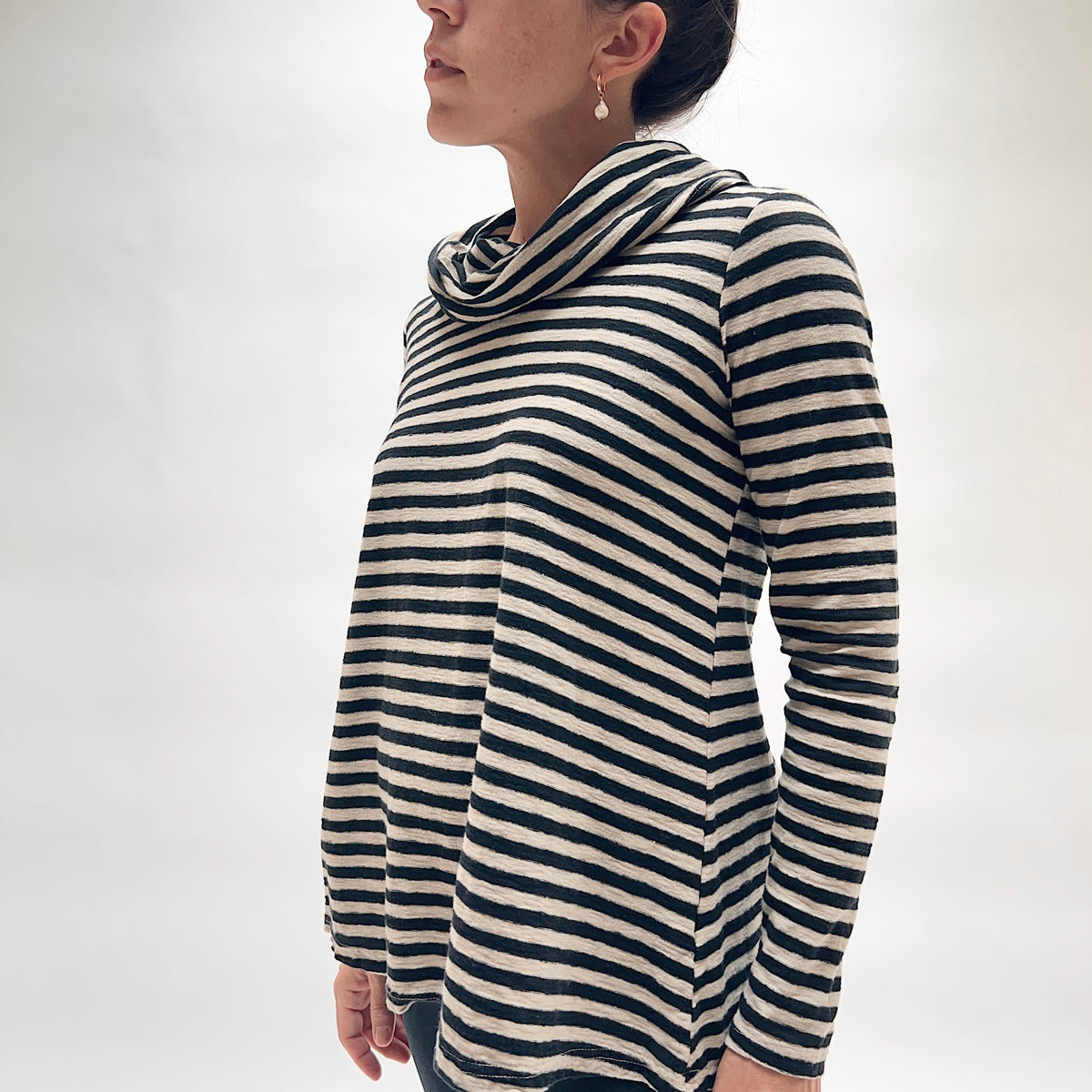 Side profile of model wearing the Cut Loose Striped Cowl Neck Pullover in Moonbeam, showing the generous draped cowl neck, tunic length, relaxed A-line silhouette, and side slit hem detail in moonbeam and black horizontal stripe cotton-linen blend
