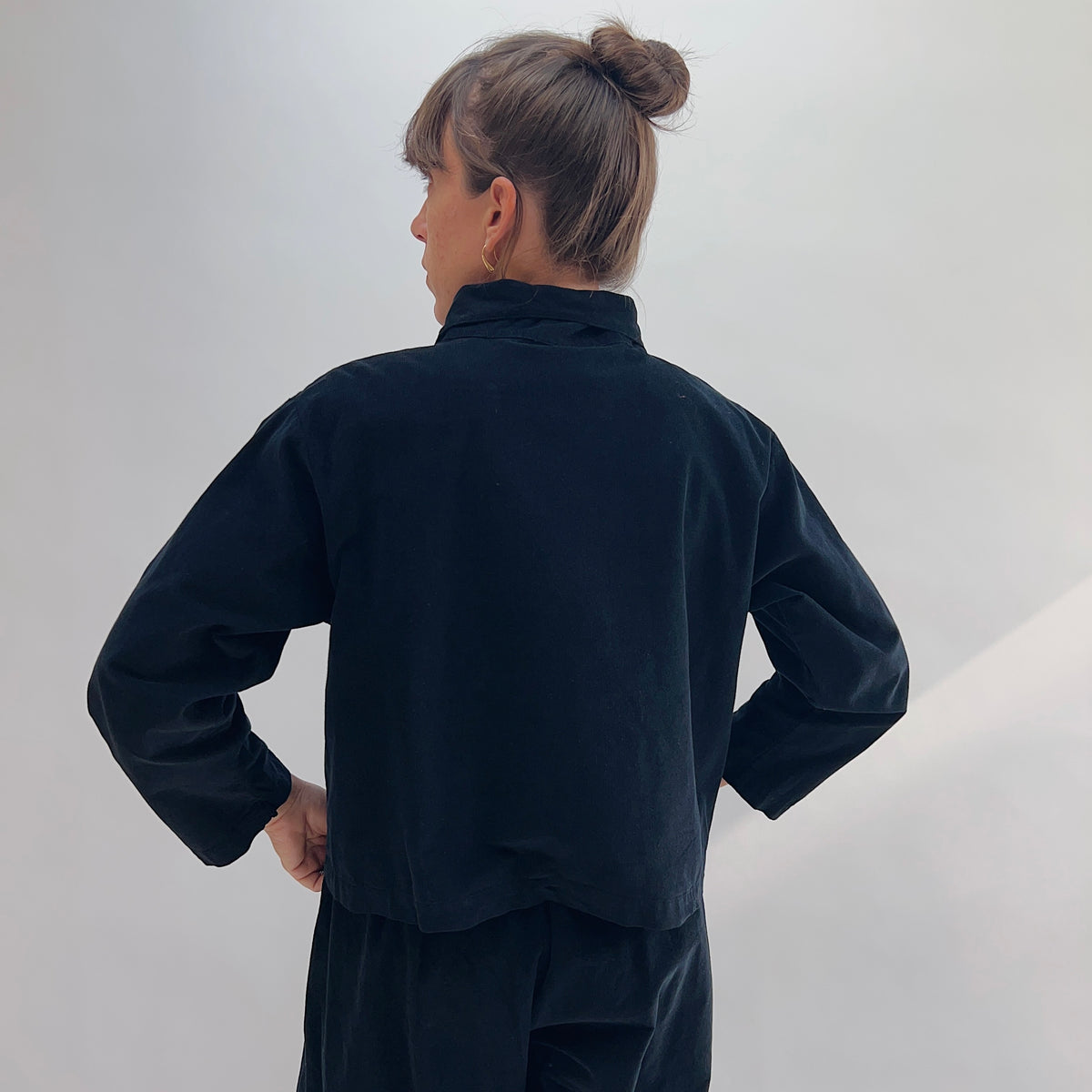 Back view of the Bryn Walker Corduroy Audrey Jacket in Black, showing cropped hemline, relaxed silhouette, and pinwheel corduroy texture, paired with black trousers
