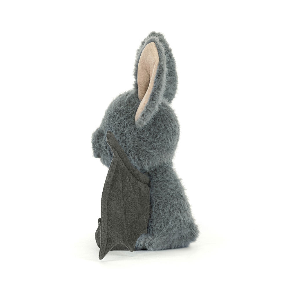 Side profile of the Jellycat Broox Bat plush toy on a white background, showing the blue-grey fluffy body, one large cream-lined ear, and a folded dark wing tucked against the body