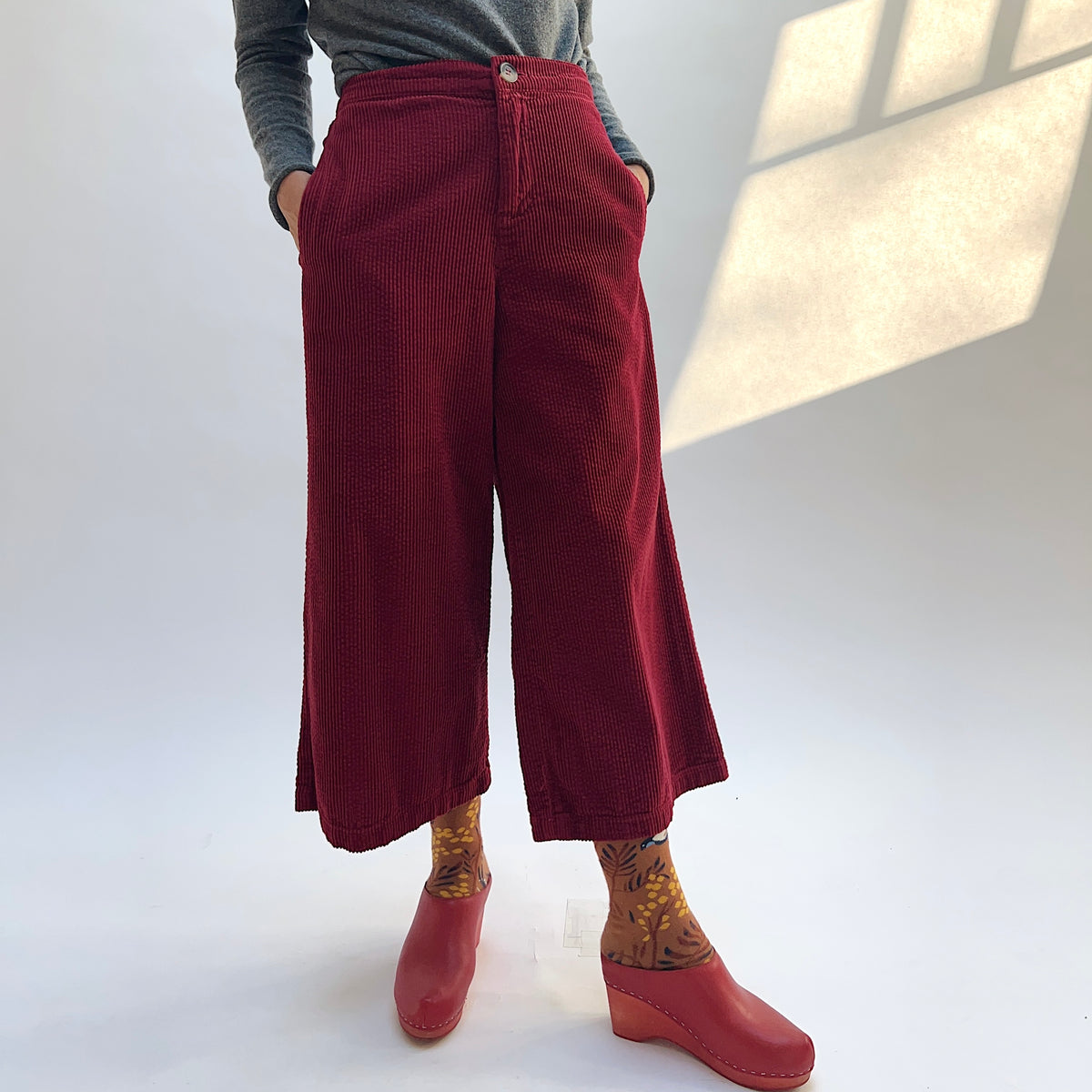 Front view of the Lux Corduroy Crop Wide Leg Pant in Maraschino with the waistband visible and the model’s hands in the side pockets.
