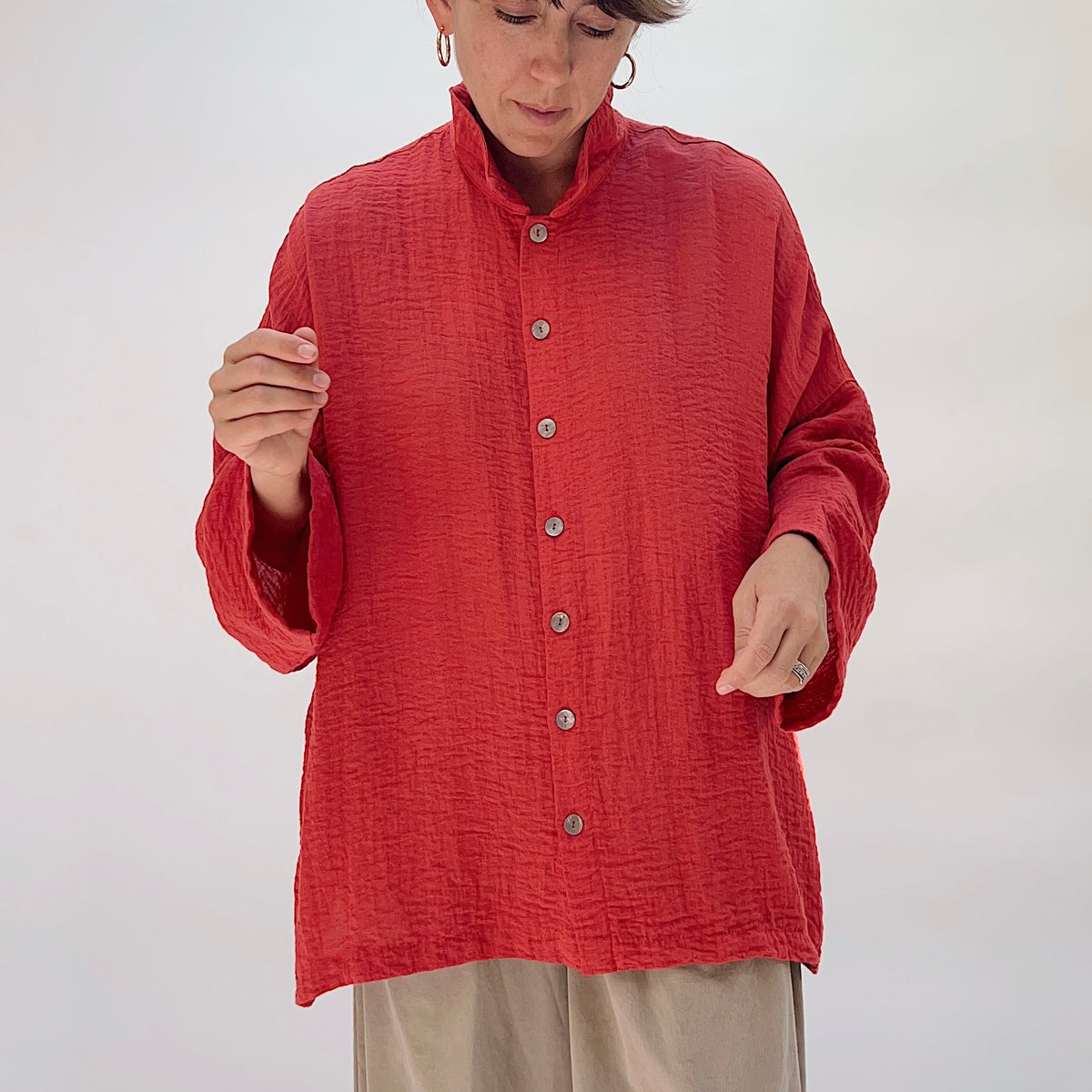 Eleven Stitch Travel Big Shirt in Pimento, front view on model looking down, showing stand collar, five wood button closure, textured pimento fabric, and relaxed boxy fit, paired with khaki trousers
