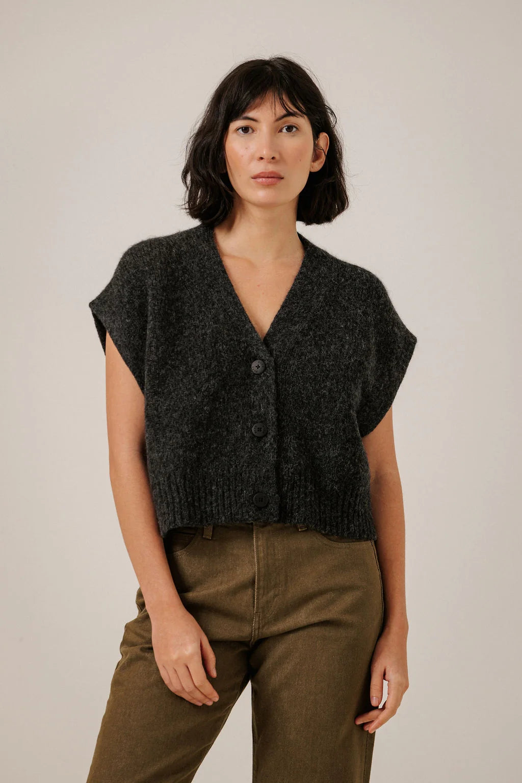 Front view of a model wearing the Bare Knitwear Basalt vest, showing its dark knit, V-neck and button front.

