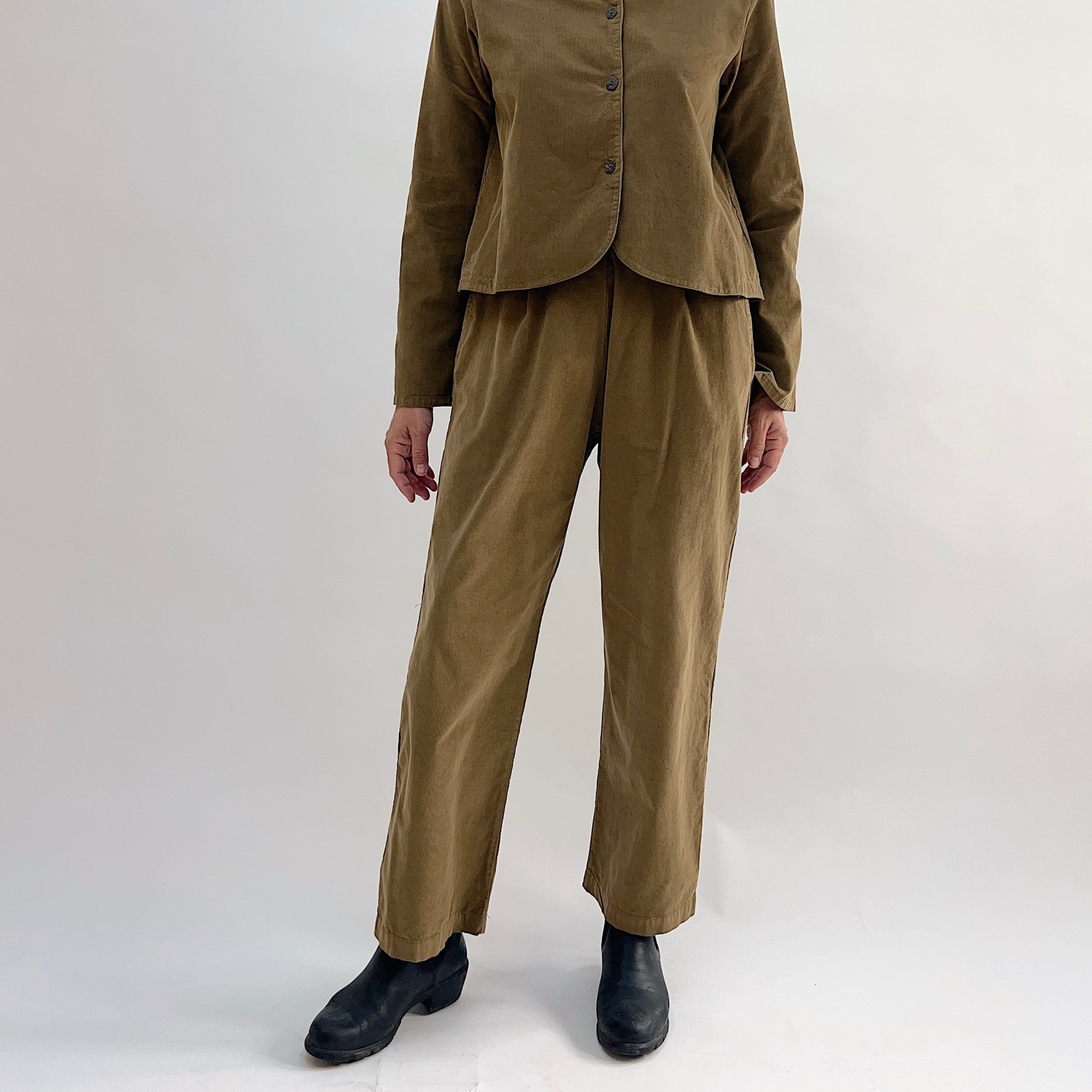 Model wearing the Bryn Walker Corduroy Pleated Pants in Partridge, full front view highlighting flat front pleats, straight leg, full-length hem, and olive pinwheel corduroy texture, styled with matching Standing Collar Crop Jacket and black Chelsea boots
