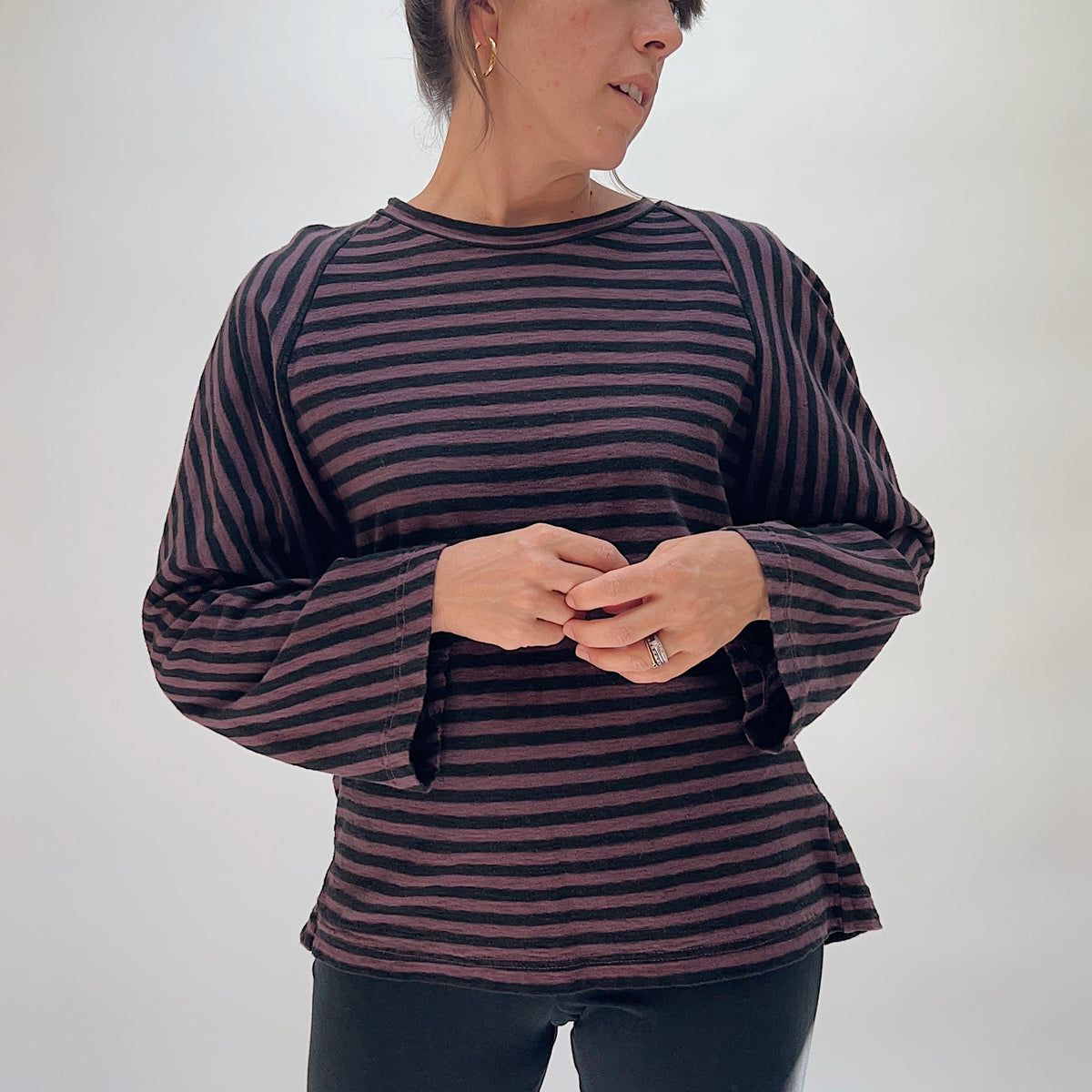 Model wearing the Cut Loose Slouchy Raglan Tee in Cinnabark Stripes from the front, showing the crew neckline, raglan seams, wide long sleeves, and oversized relaxed fit in horizontal cinnabark and black stripe cotton-linen fabric
