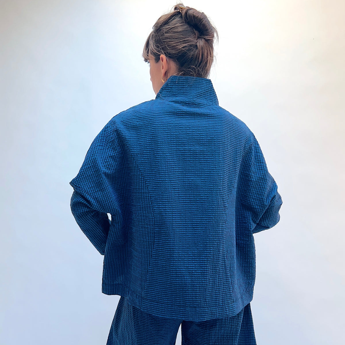 Niche Sofi Top in Blue Seersucker Stripe, back view showing the relaxed boxy silhouette and high funnel neck in teal and black seersucker stripe
