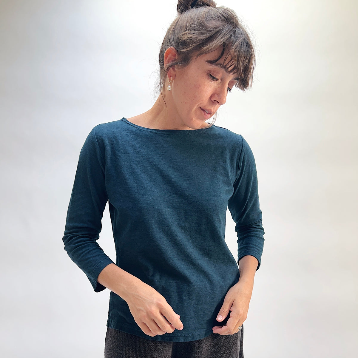 Model wearing the Cut Loose 3/4 Sleeve Boatneck Top in Etan, close-up three-quarter view looking down, deep teal cotton-linen boatneck top with 3/4 sleeves and subtle slub texture, styled with black textured pants
