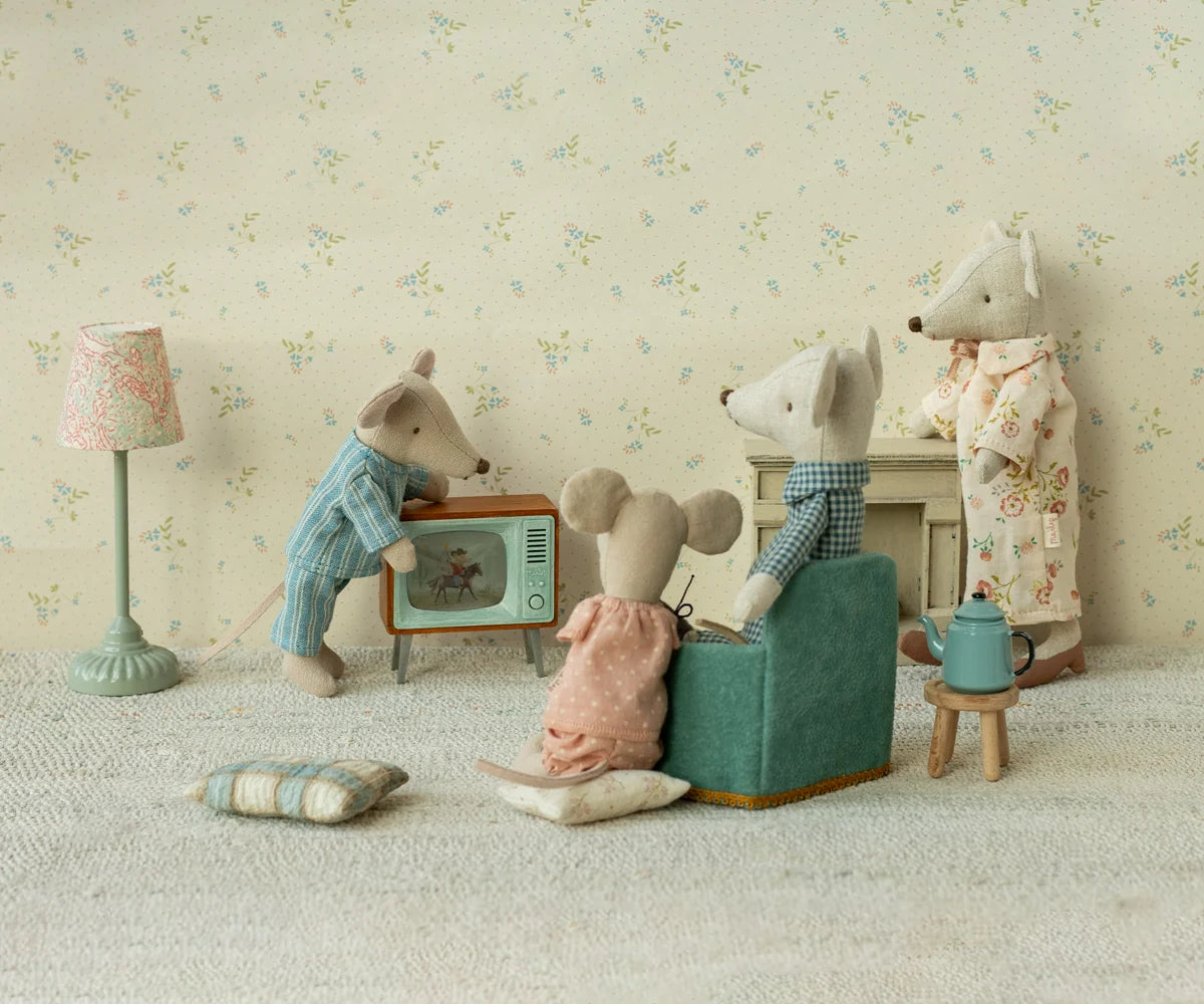 Maileg Mouse Television Set — lifestyle scene of three Maileg mouse dolls in pajamas gathered in a cosy living room around the miniature television, with a pink floor lamp, teal armchair, and miniature teakettle

