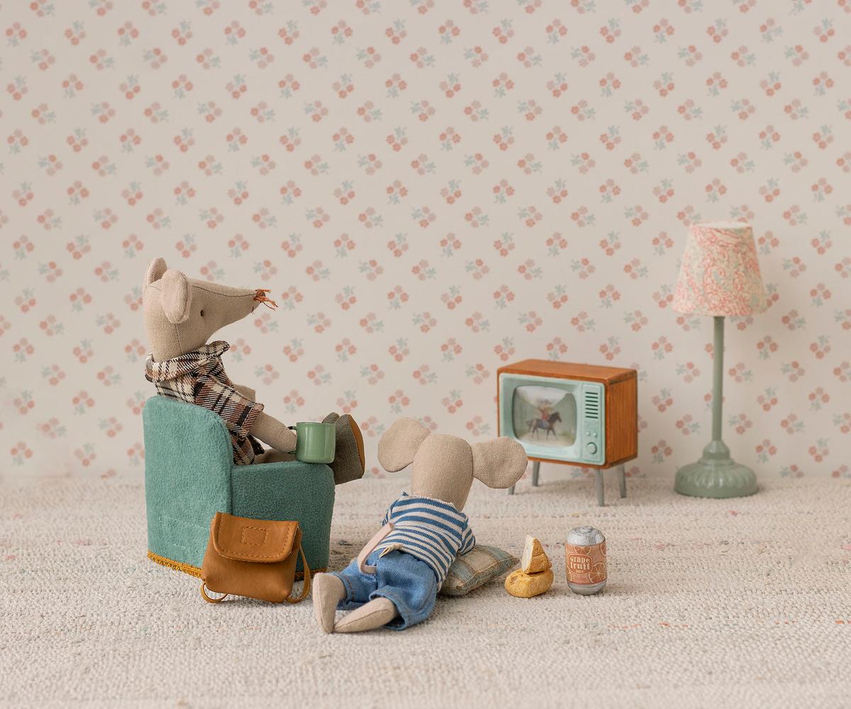 Maileg Mouse Television Set — lifestyle scene of two Maileg mouse dolls relaxing in a dollhouse living room with the miniature television and pink floor lamp, one mouse seated in a teal armchair holding a mug
