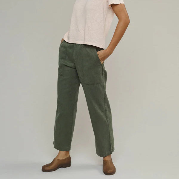 Woman wearing a light pink top and green pants on a plain background