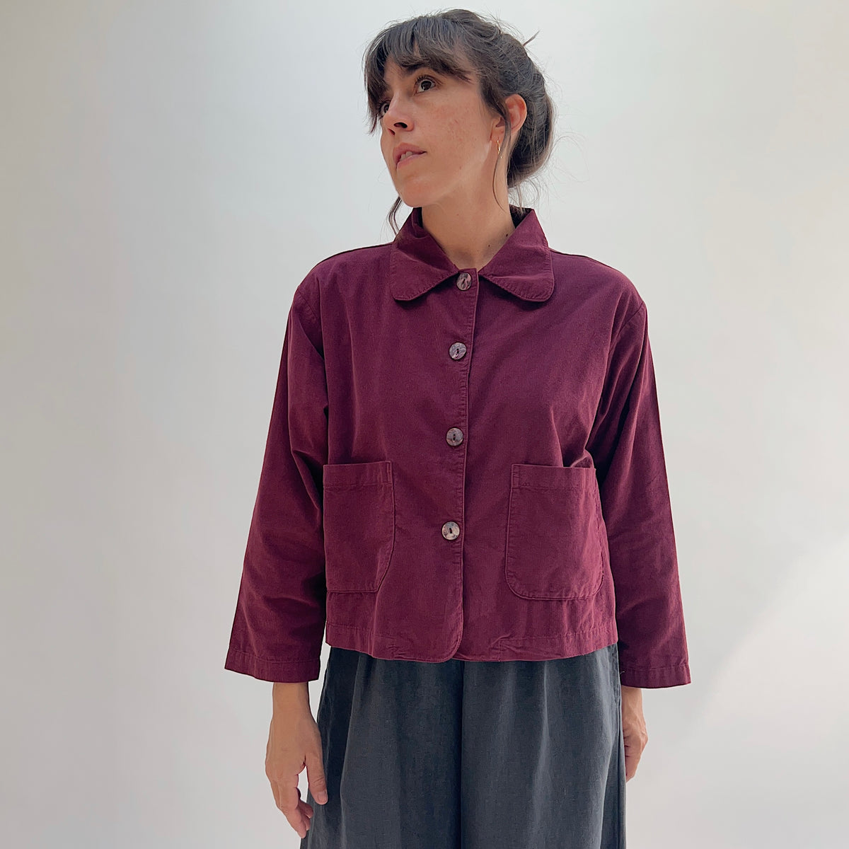 Model wearing the Bryn Walker Corduroy Audrey Jacket in Rhone, full front view showing rounded collar, shell button closure, patch pockets, and relaxed cropped silhouette, paired with grey skirt
