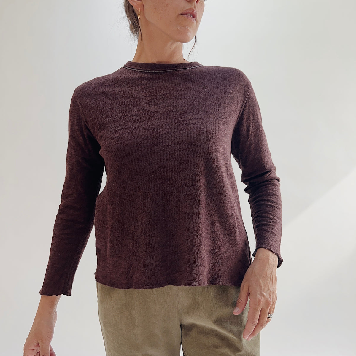 Model wearing the Bryn Walker Double Cotton Tee in Chicory, full front view highlighting raw-edge crew neckline, raw-hem sleeve cuffs, relaxed silhouette, and double-layer cotton texture in deep chicory burgundy, styled with olive pants
