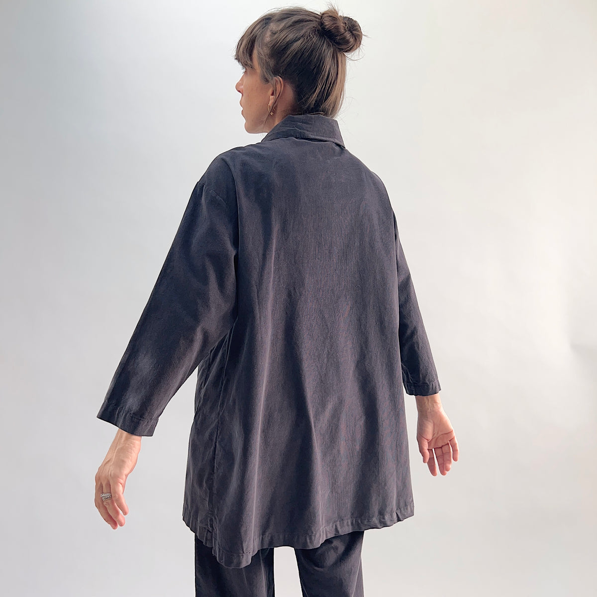 Back view of model wearing the Bryn Walker Corduroy Car Coat in Fig, showing rounded collar, relaxed A-line silhouette, 3/4 sleeves, and deep fig pinwheel corduroy, styled with matching corduroy pants
