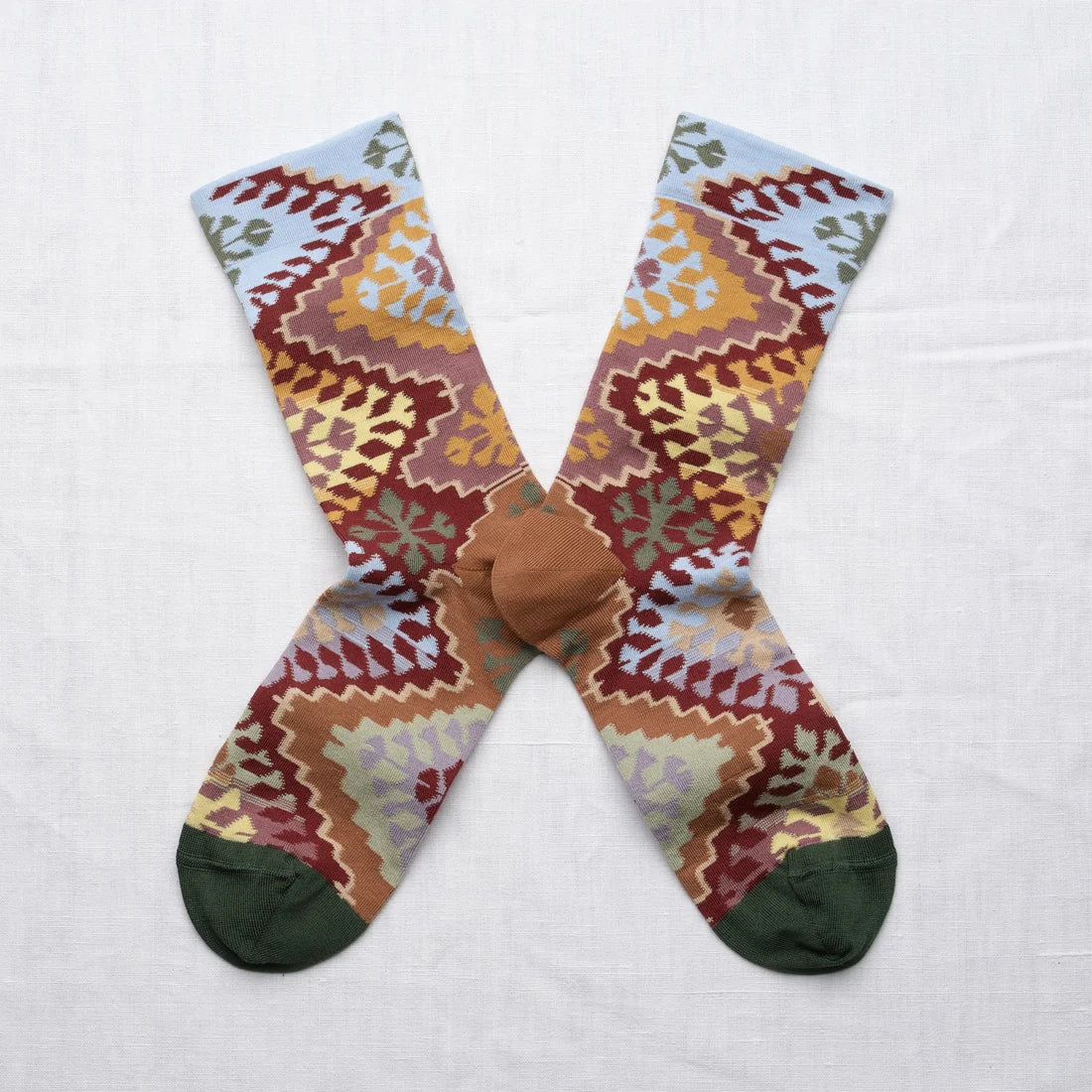 Bonne Maison Le Tapis Multicolor Socks, flat lay pair showing the kilim-inspired geometric pattern in burgundy, ochre, dusty rose, sage, and sky blue with dark green toe
