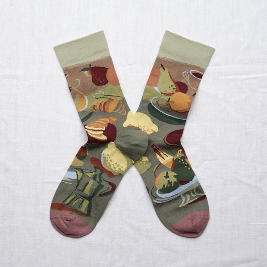 Bonne Maison Le Brunch Socks, flat lay pair showing the illustrated brunch tableau with coffee cups, croissants, fruit, and cheese in olive, burgundy, and ochre with dusty rose heel and toe
