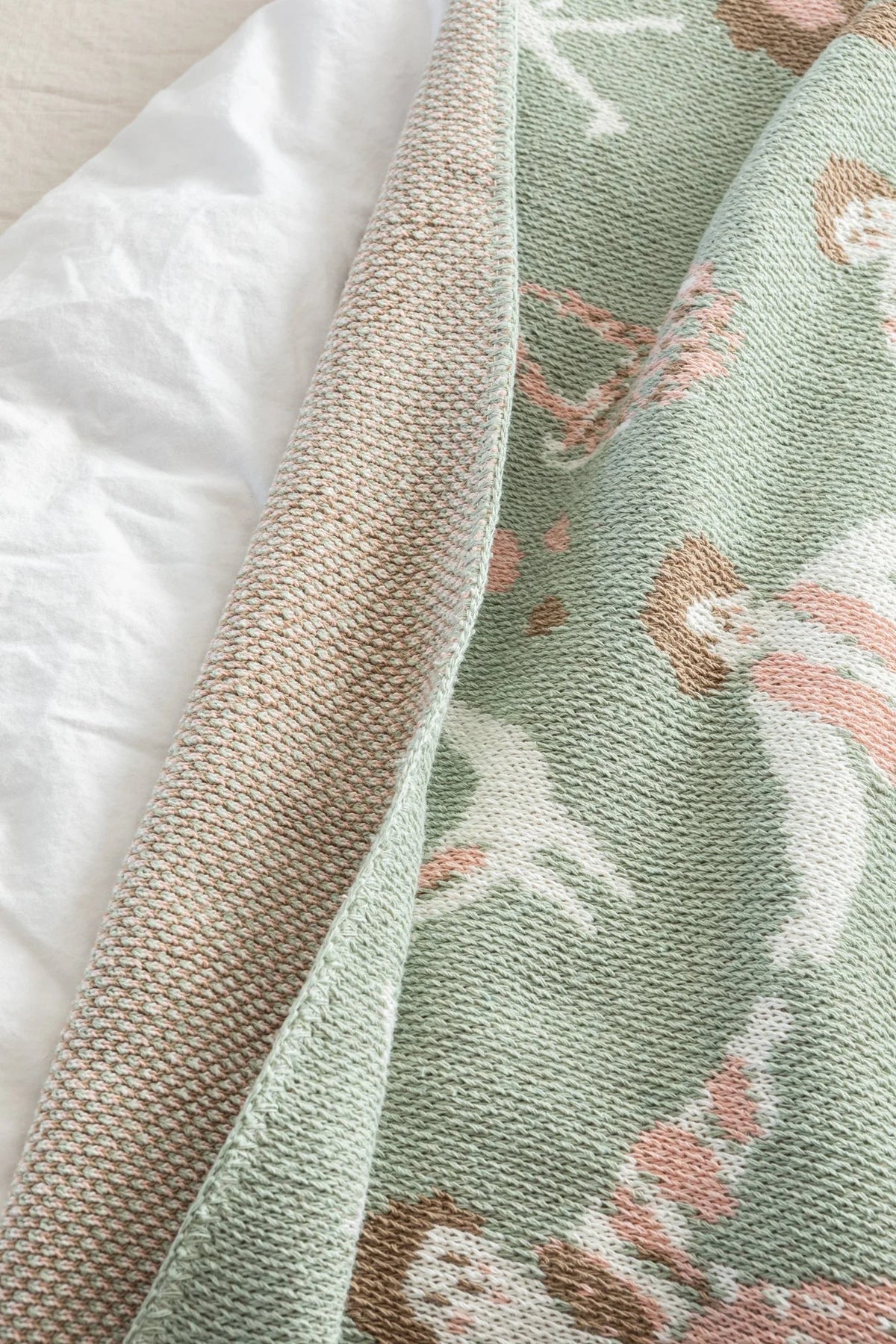 Close-up of the Forest Friends Sky blanket’s pale green knit, pink and white motifs, and folded textured reverse.
