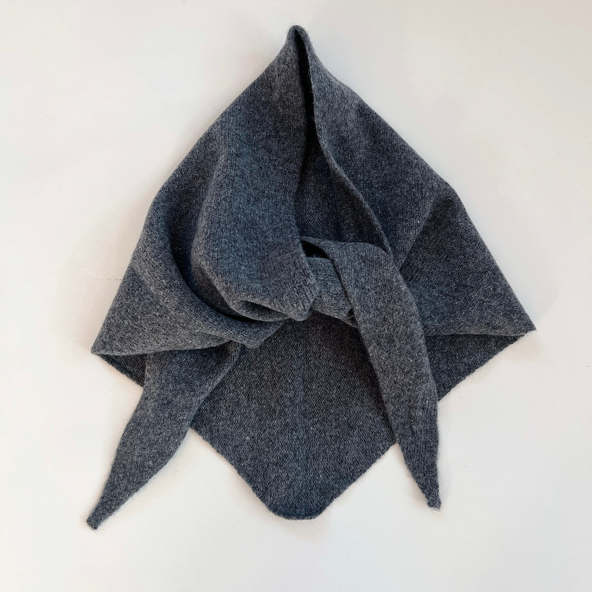 Flat lay view of the Charcoal merino wool triangle scarf arranged with a loose knot and pointed ends.
