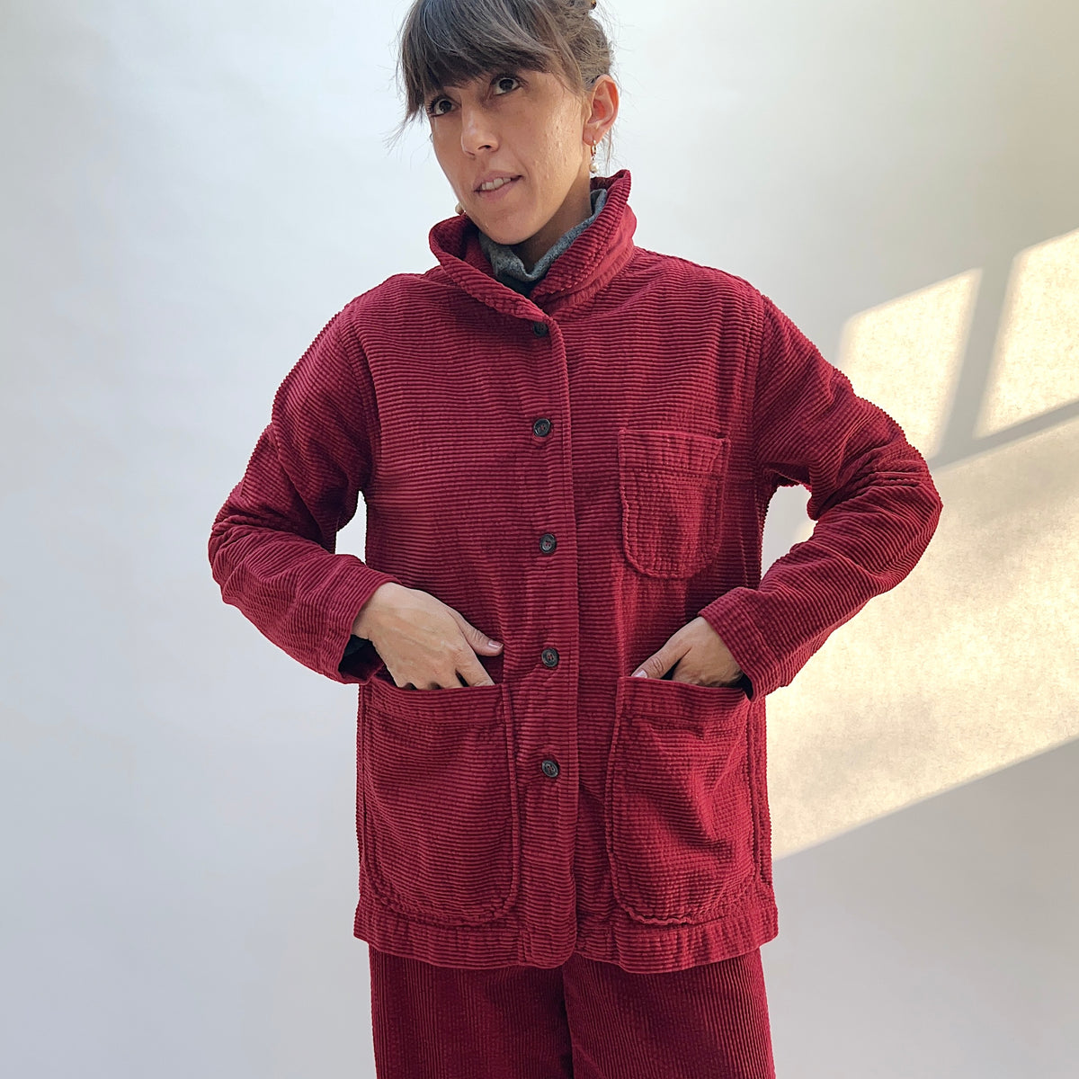 Closer front view of the Lux Corduroy Long Blazer in Maraschino, with the model’s hands in the two lower patch pockets and a chest pocket above.
