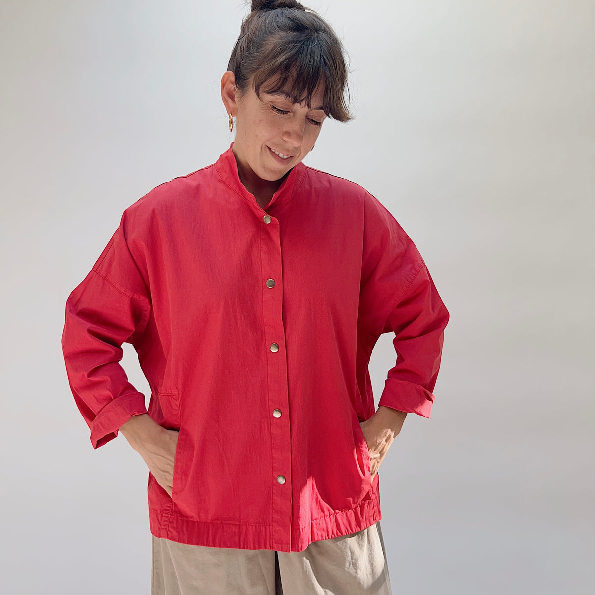 Eleven Stitch Stand Collar Jacket in Cayenne, full front view on model with hands in pockets, showing stand collar, metal snap closures, two front pockets, and elasticated hem detail, paired with khaki wide-leg trousers
