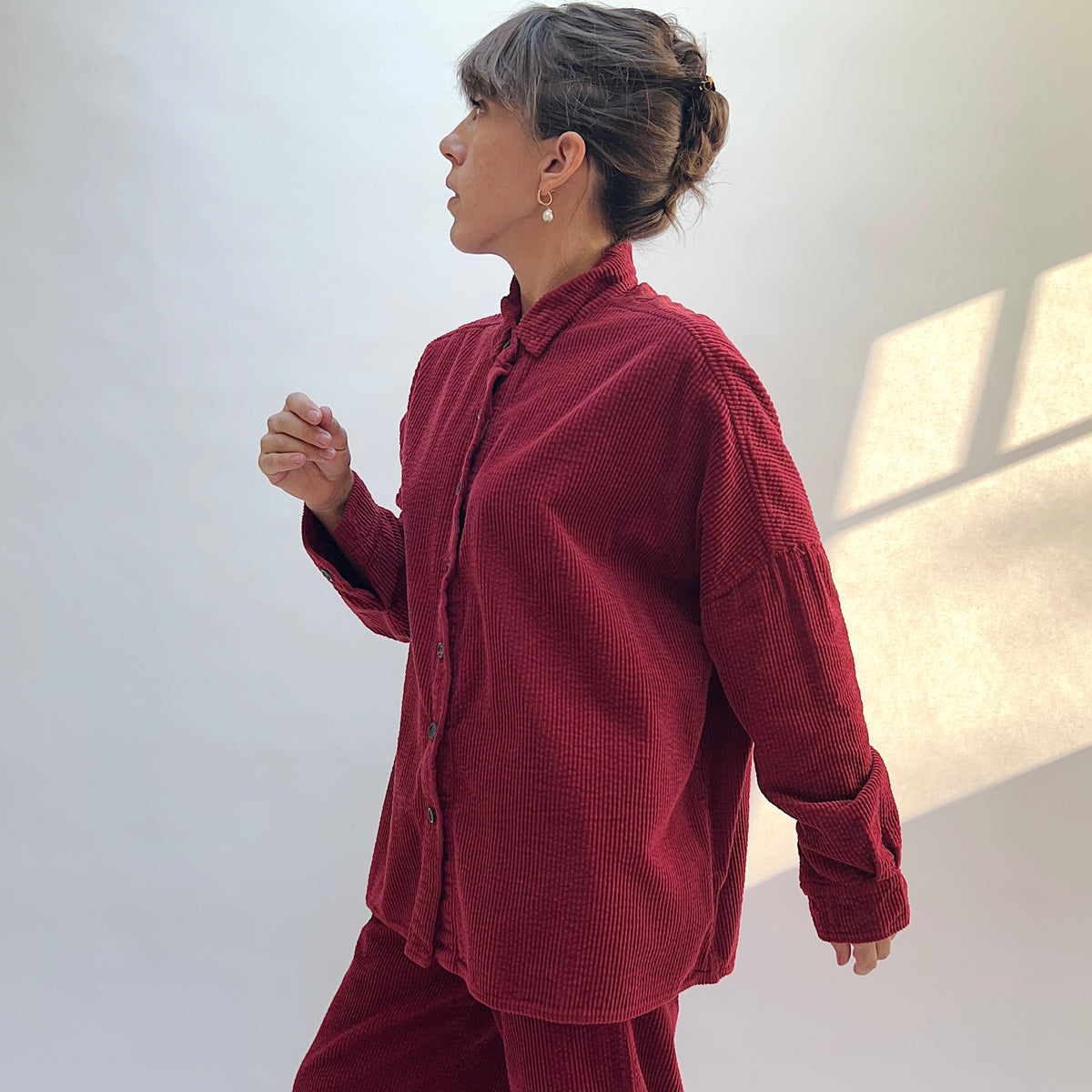 Side view of the Lux Corduroy Oversized Shirt in Maraschino on a model, showing the dropped shoulders, long sleeves, and curved hem.
