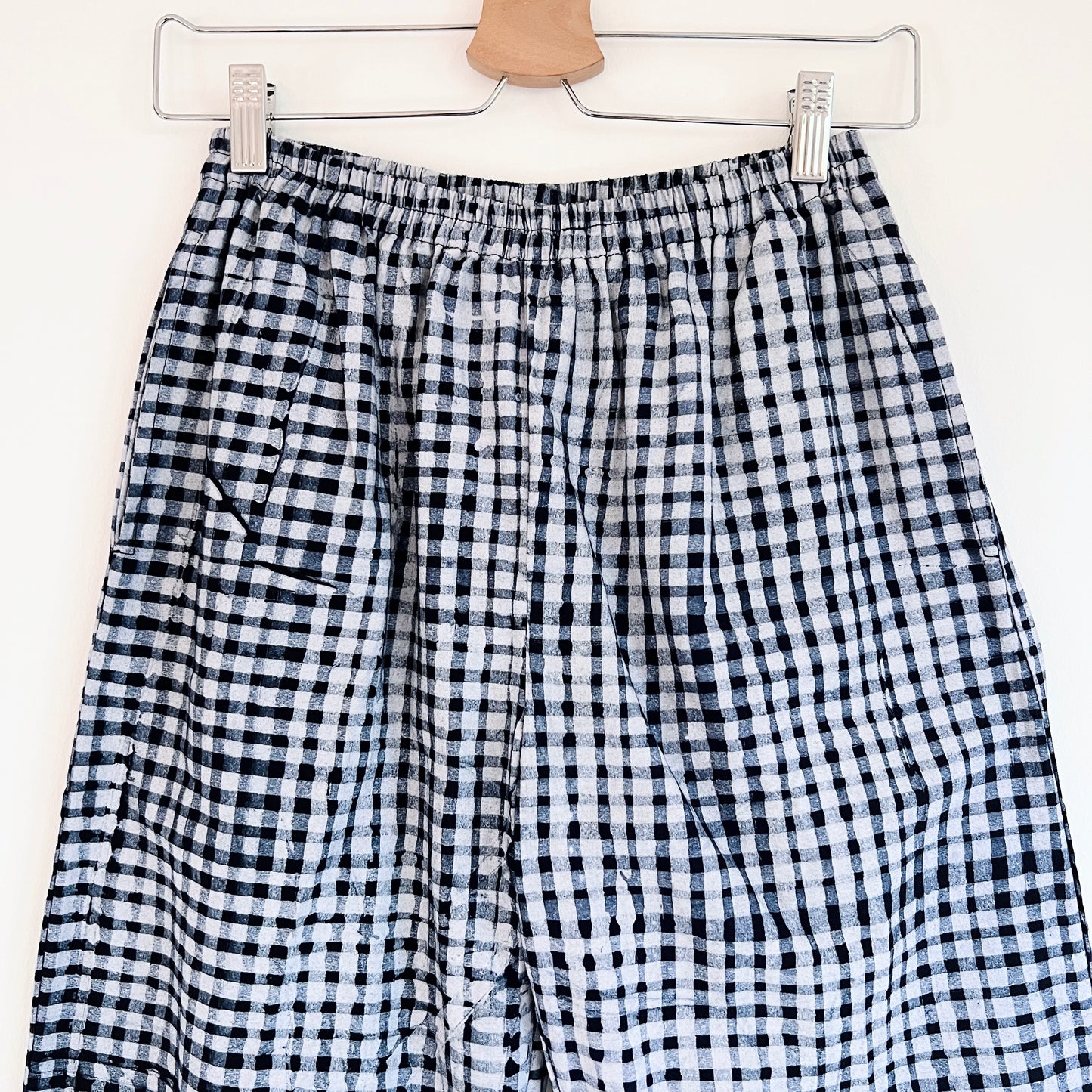 Close-up of the waistband and upper leg of the Lazy Pants in Indigo Gingham, showing the elastic waistband, side pocket opening, and hand-printed black and white gingham check pattern with natural Batiki dye variation

