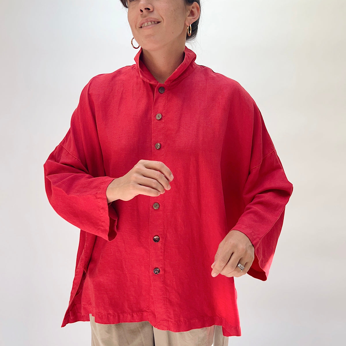 Eleven Stitch Linen Blend Big Shirt in Cayenne, front view on smiling model with hands clasped, showing stand collar, five wood button closure, textured cayenne linen-blend fabric, and relaxed oversized fit, paired with khaki trousers
